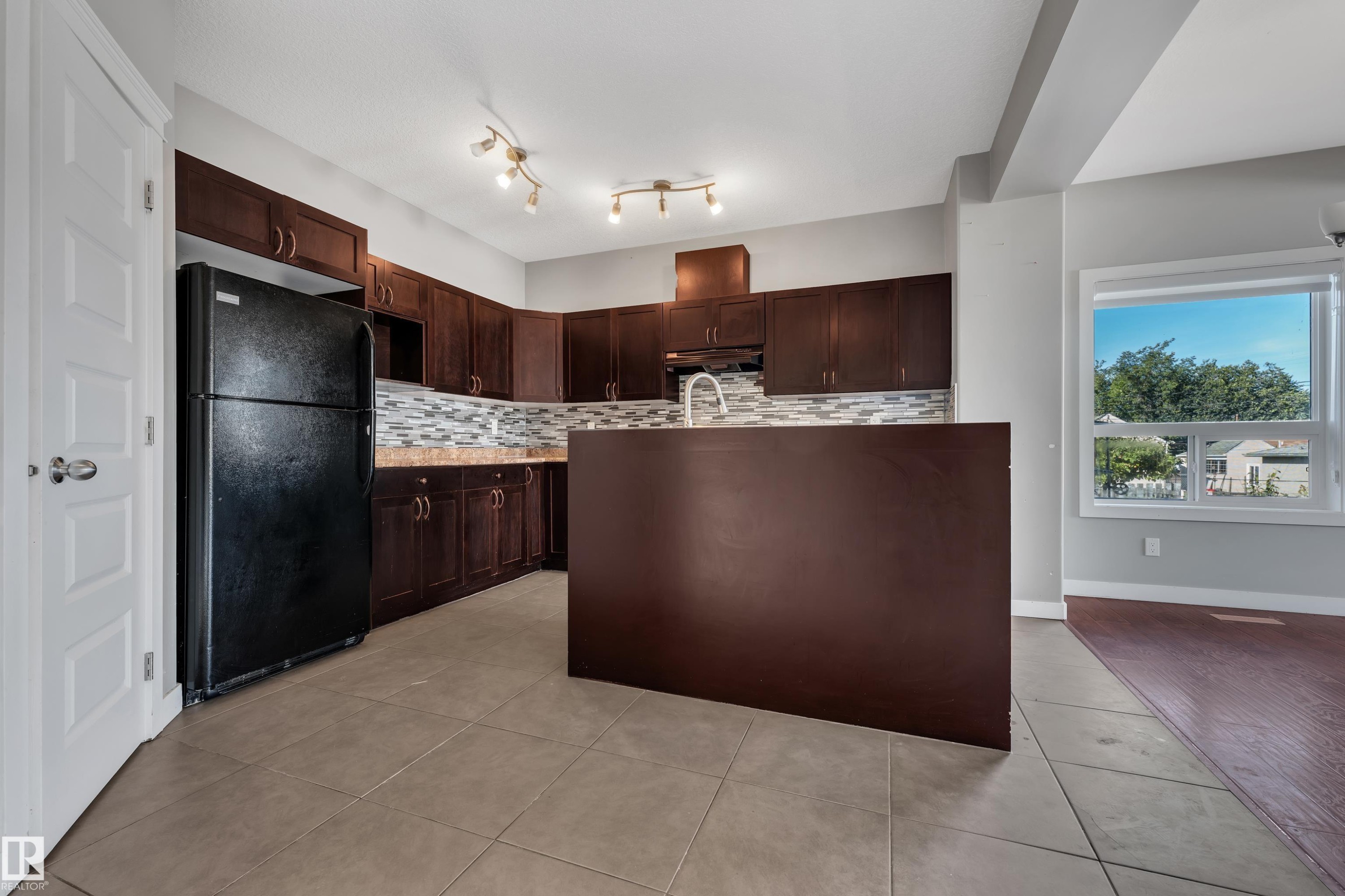 Kitchen featuring dark wood-finish cabinetry, tile backsplash, stainless steel sink, track lighting, and a kitchen island - 11421 82 Street Nw, Edmonton, AB