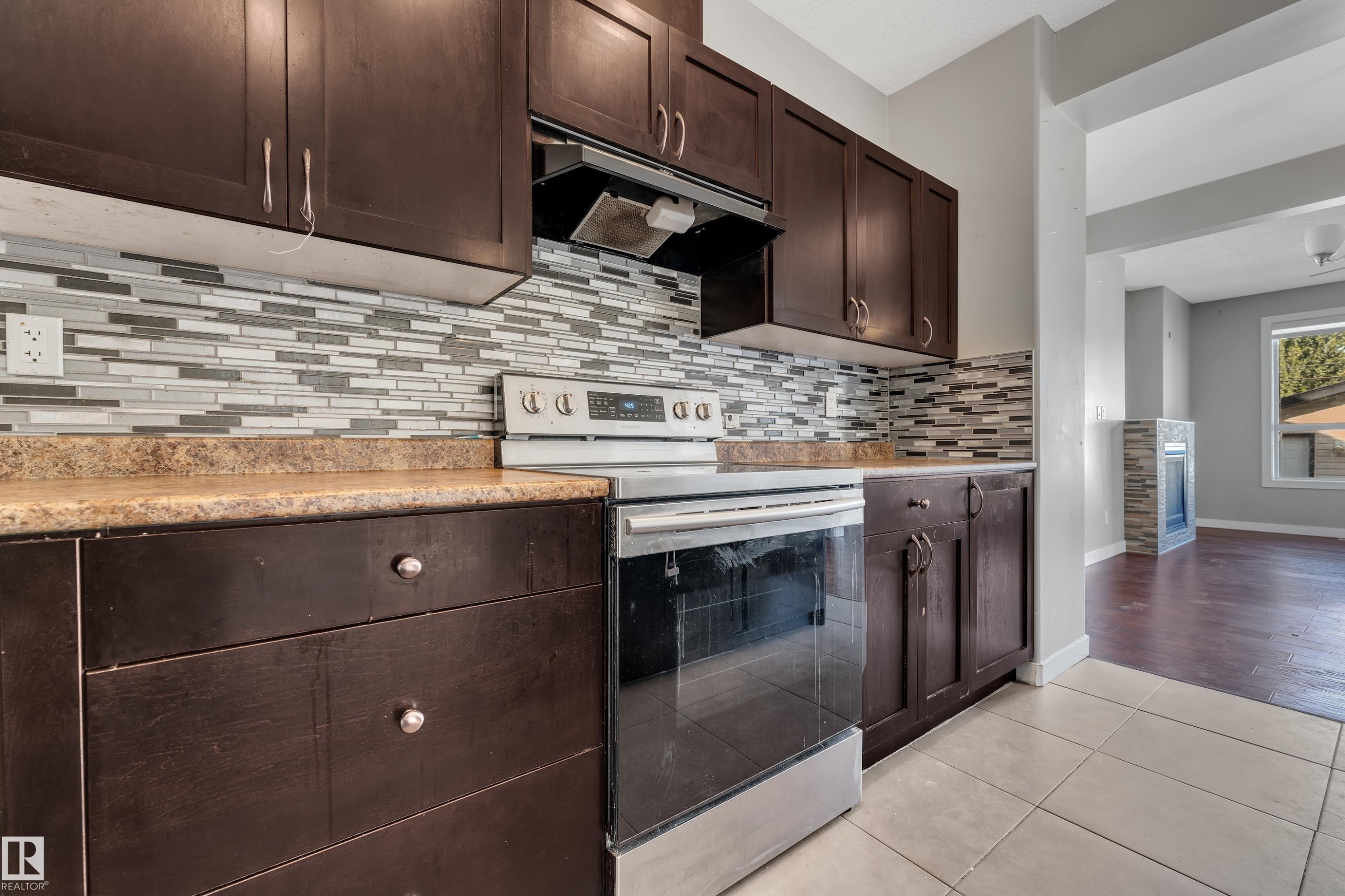 Dark wood-finish cabinetry with silver-tone hardware, a light-toned countertop, and a mosaic tile backsplash - 11421 82 Street Nw, Edmonton, AB