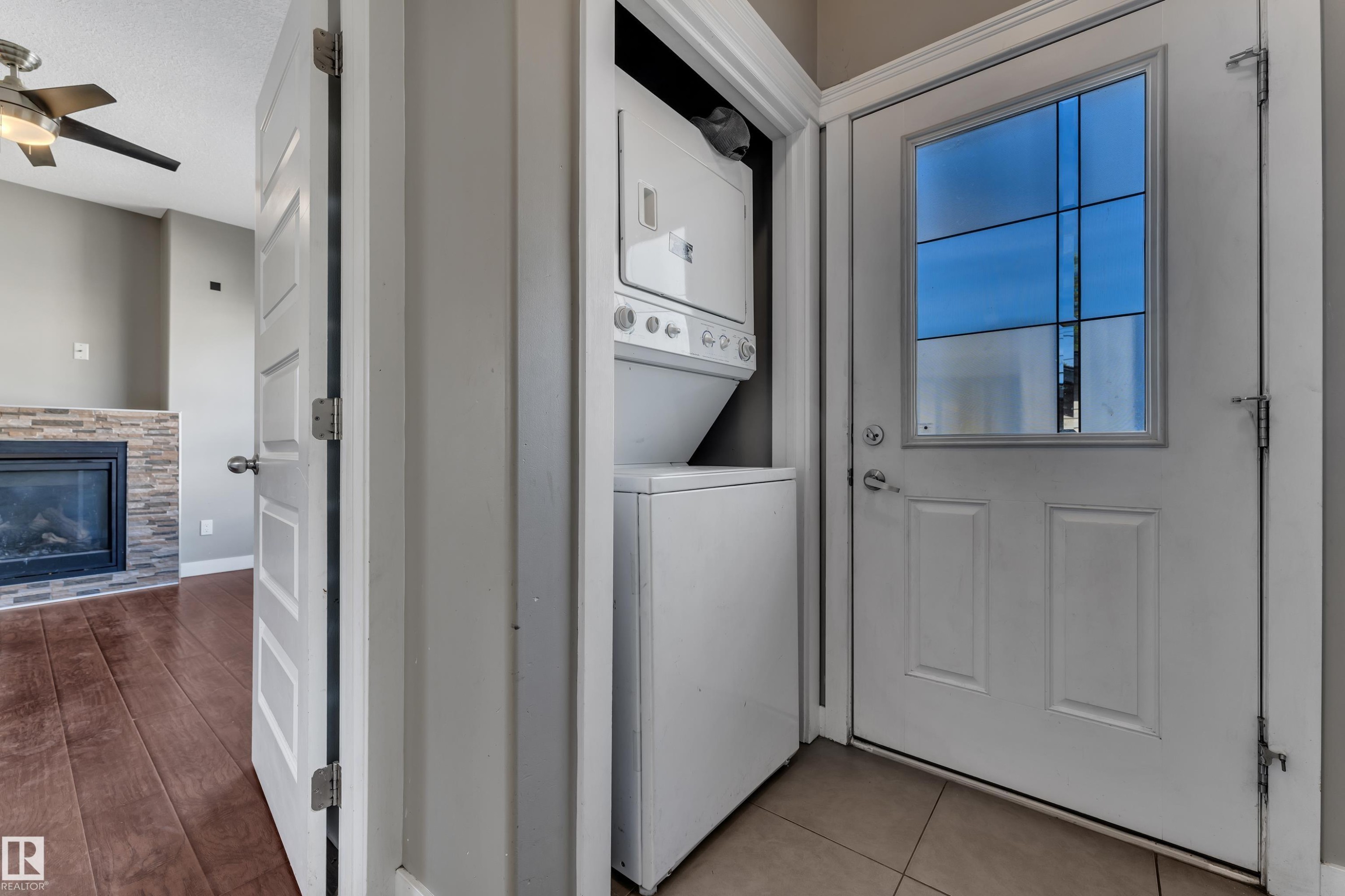 Convenient laundry closet featuring a stacked washer and dryer unit, ceramic tile flooring, and direct access to the main living areas - 11421 82 Street Nw, Edmonton, AB