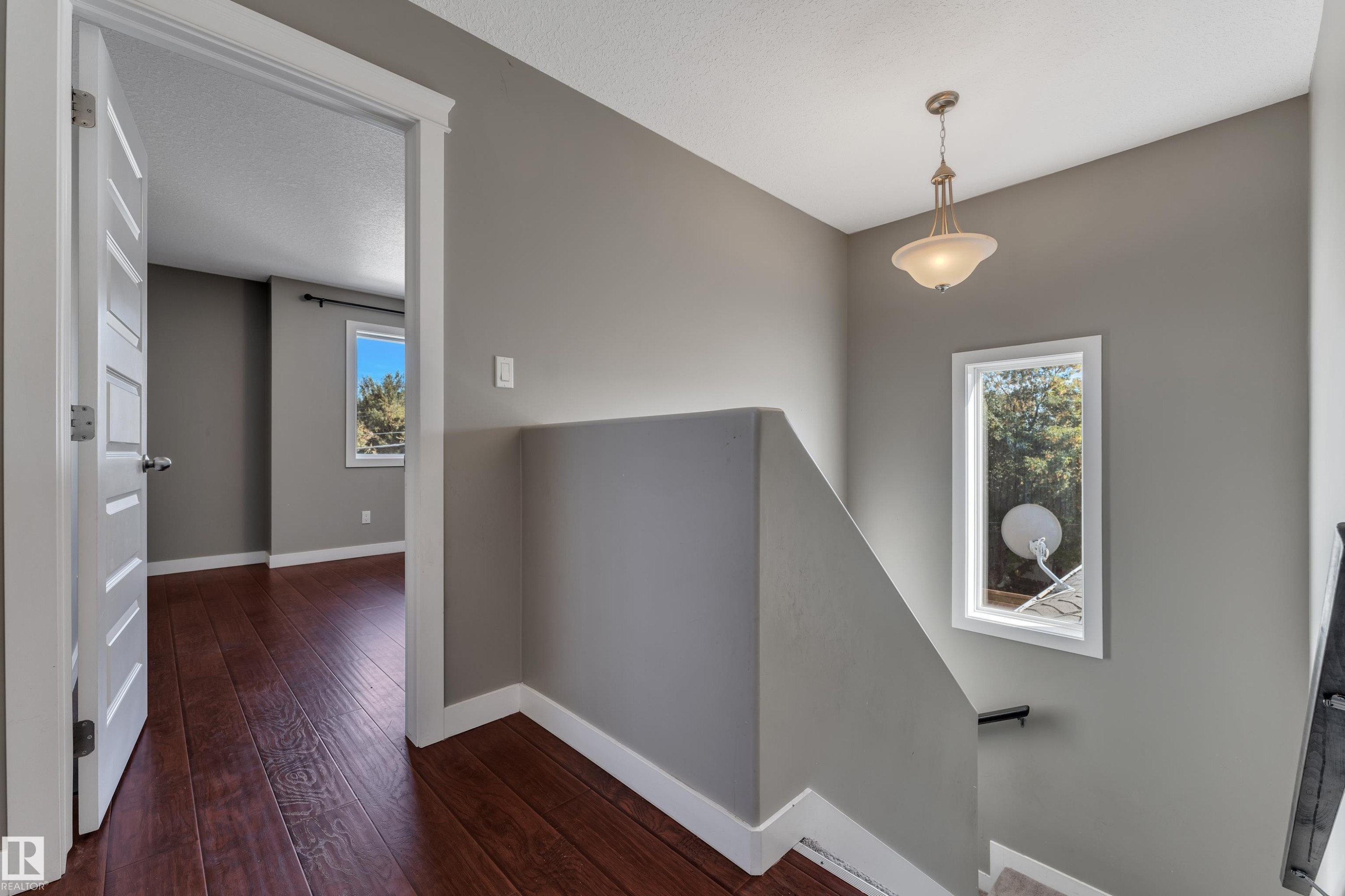 Hallway featuring wood-finish flooring, a white paneled door, and a decorative pendant light fixture - 11421 82 Street Nw, Edmonton, AB