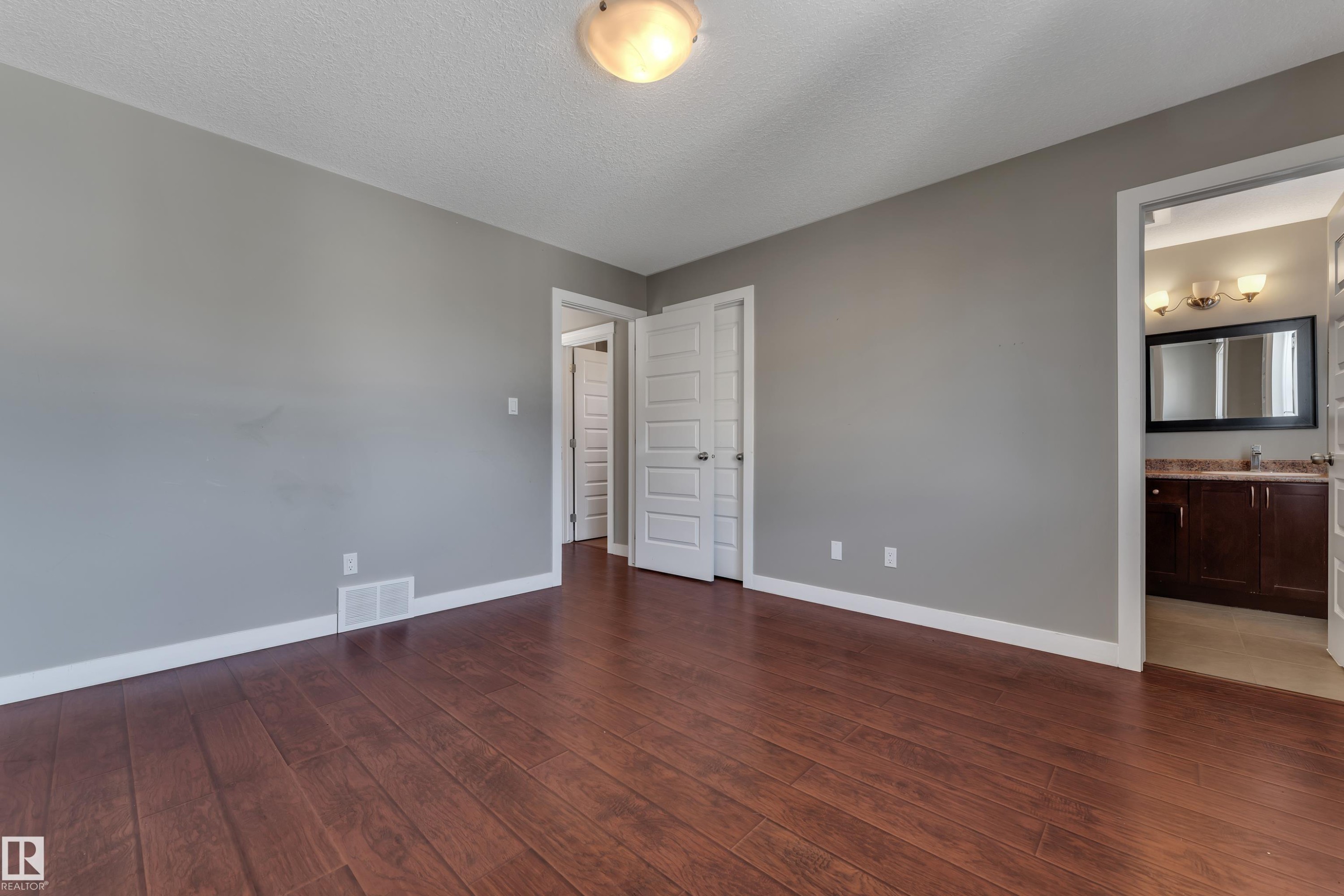 Spacious bedroom with warm wood-finish flooring, neutral gray walls, and abundant natural light from recessed ceiling fixture - 11421 82 Street Nw, Edmonton, AB