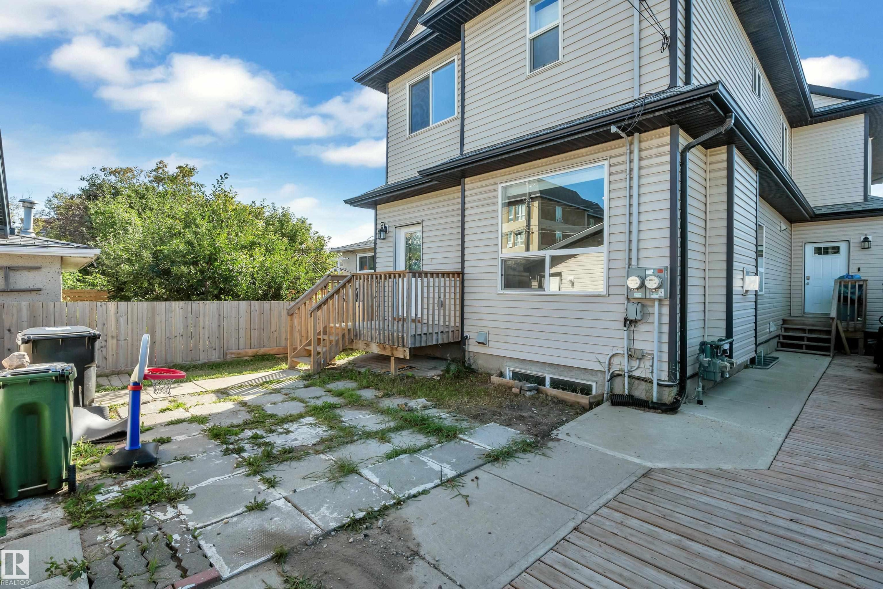 Exterior featuring vinyl siding, a wooden privacy fence, a ground-level patio, a wooden deck, and a concrete walkway - 11421 82 Street Nw, Edmonton, AB
