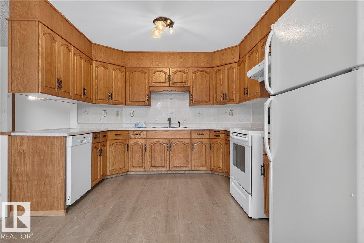 U-shaped kitchen with wood-finish cabinetry, light-toned countertops, tile backsplash, and light wood-finish flooring - 2907 49 Street Nw, Edmonton, AB