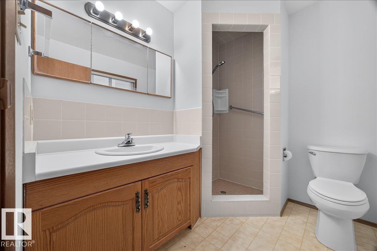 Bathroom featuring a wood-finish vanity with an integrated sink, white countertop, and tiled backsplash - 2907 49 Street Nw, Edmonton, AB
