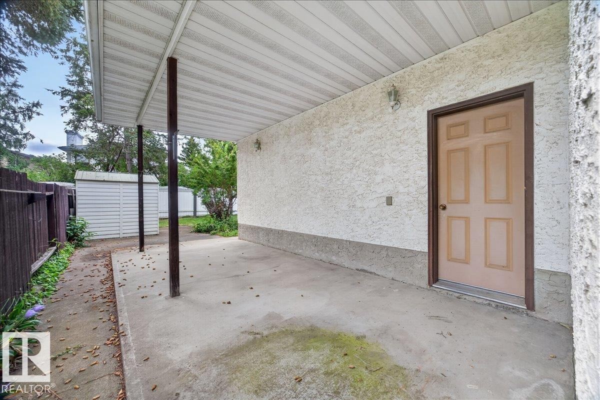 Covered concrete patio with stucco exterior, paneled door, exterior wall lighting, and a partial privacy fence - 2907 49 Street Nw, Edmonton, AB