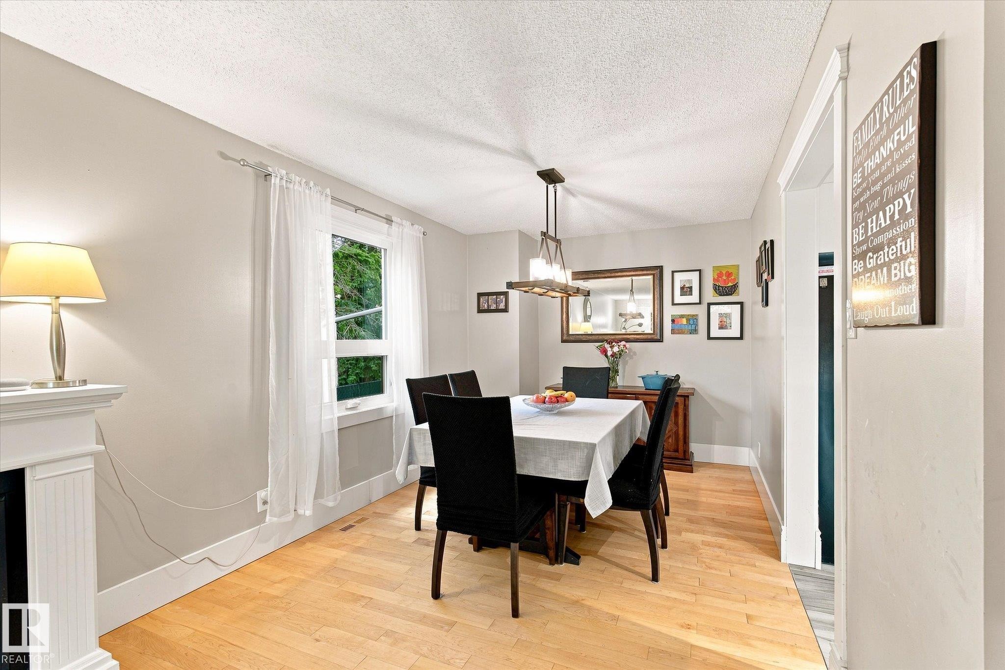 Light-filled interior space featuring wood-finish flooring, a contemporary chandelier, and a built-in mantelpiece - 3 Akins Drive, St. Albert, AB