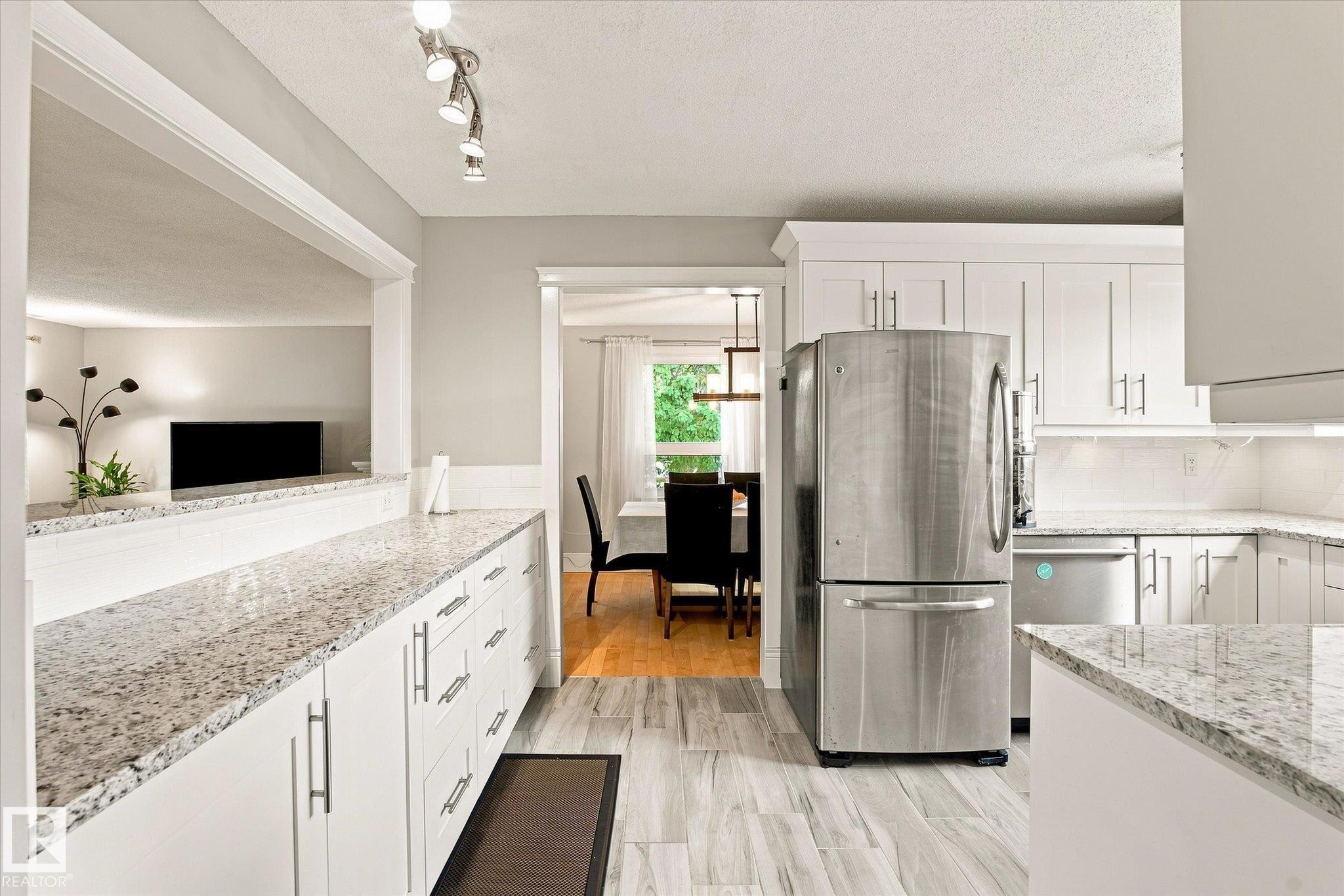White shaker-style cabinetry with stainless steel hardware, light-toned granite countertops, stainless steel appliances, and wood-finish flooring - 3 Akins Drive, St. Albert, AB