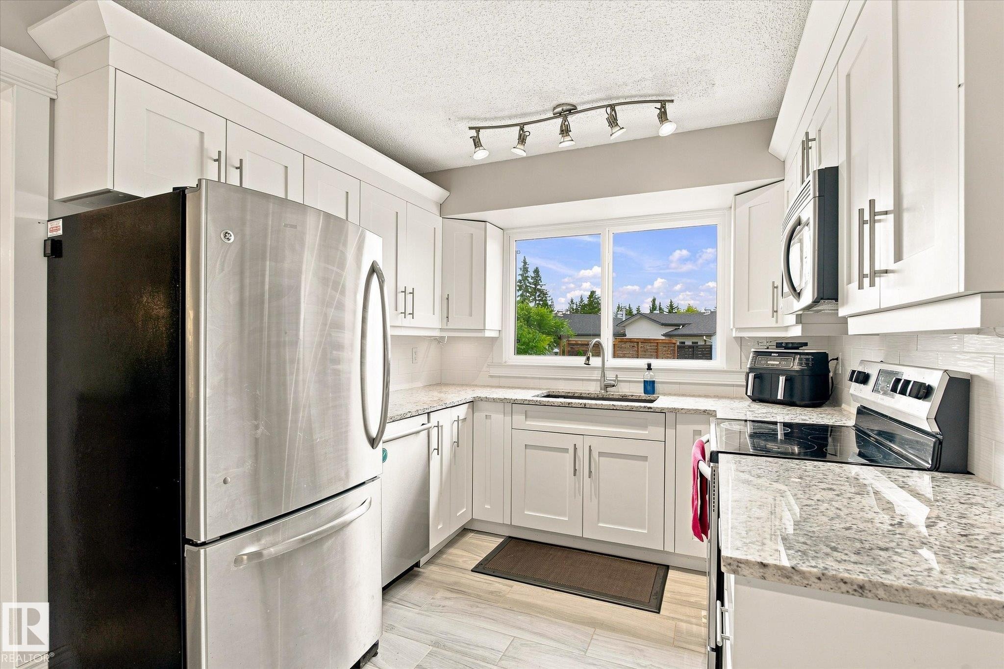 Bright kitchen with white cabinetry, stainless steel appliances, granite countertops, and a subway tile backsplash - 3 Akins Drive, St. Albert, AB