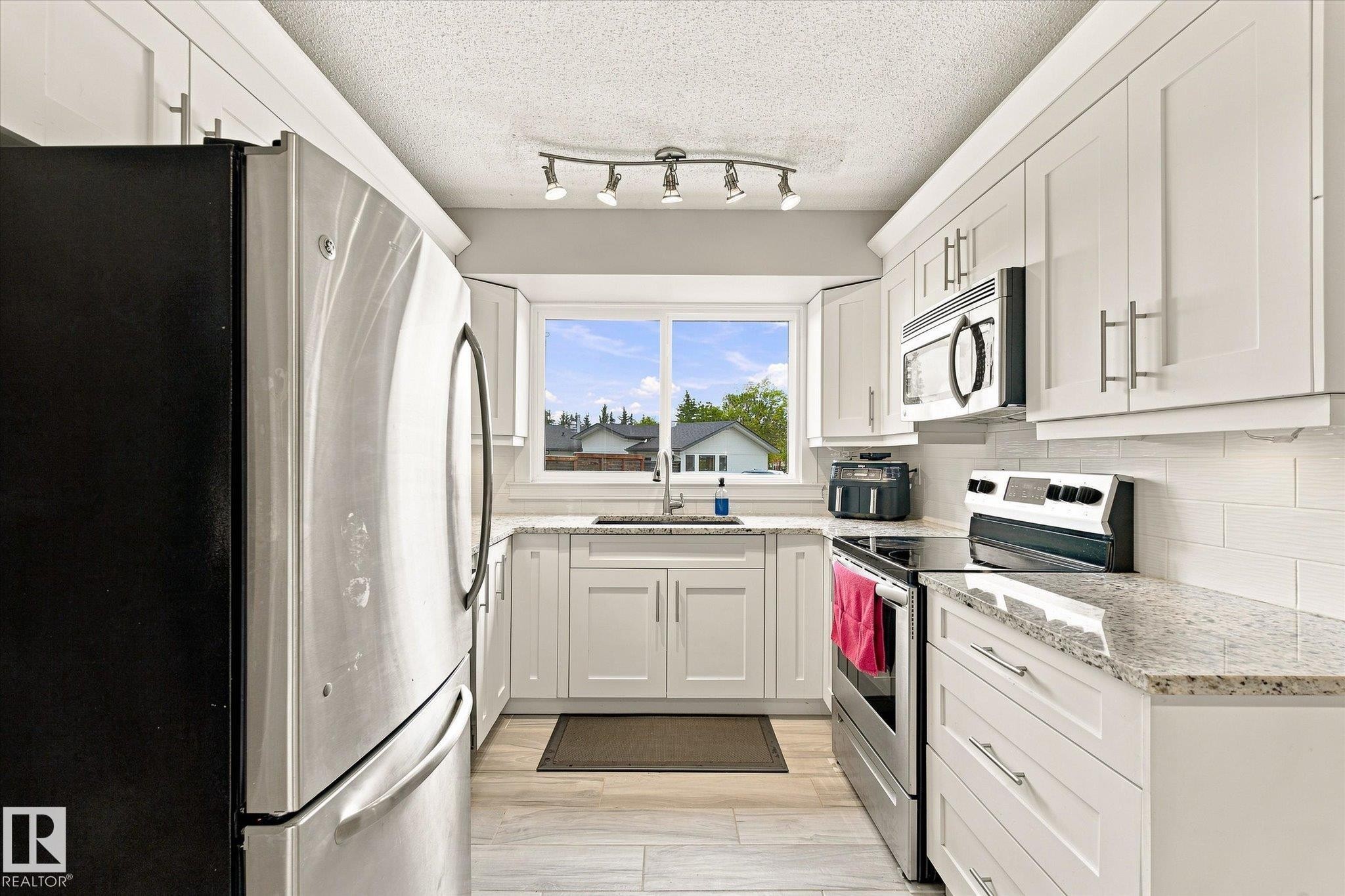 White shaker cabinetry, stainless steel appliances, light-toned wood-finish flooring, undermount sink, and track lighting - 3 Akins Drive, St. Albert, AB