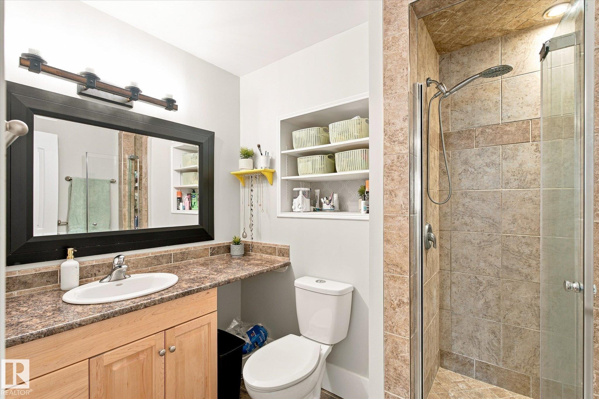 Built-in shower with glass enclosure, wood-finish vanity with counter space, framed mirror, and recessed wall shelving - 3 Akins Drive, St. Albert, AB