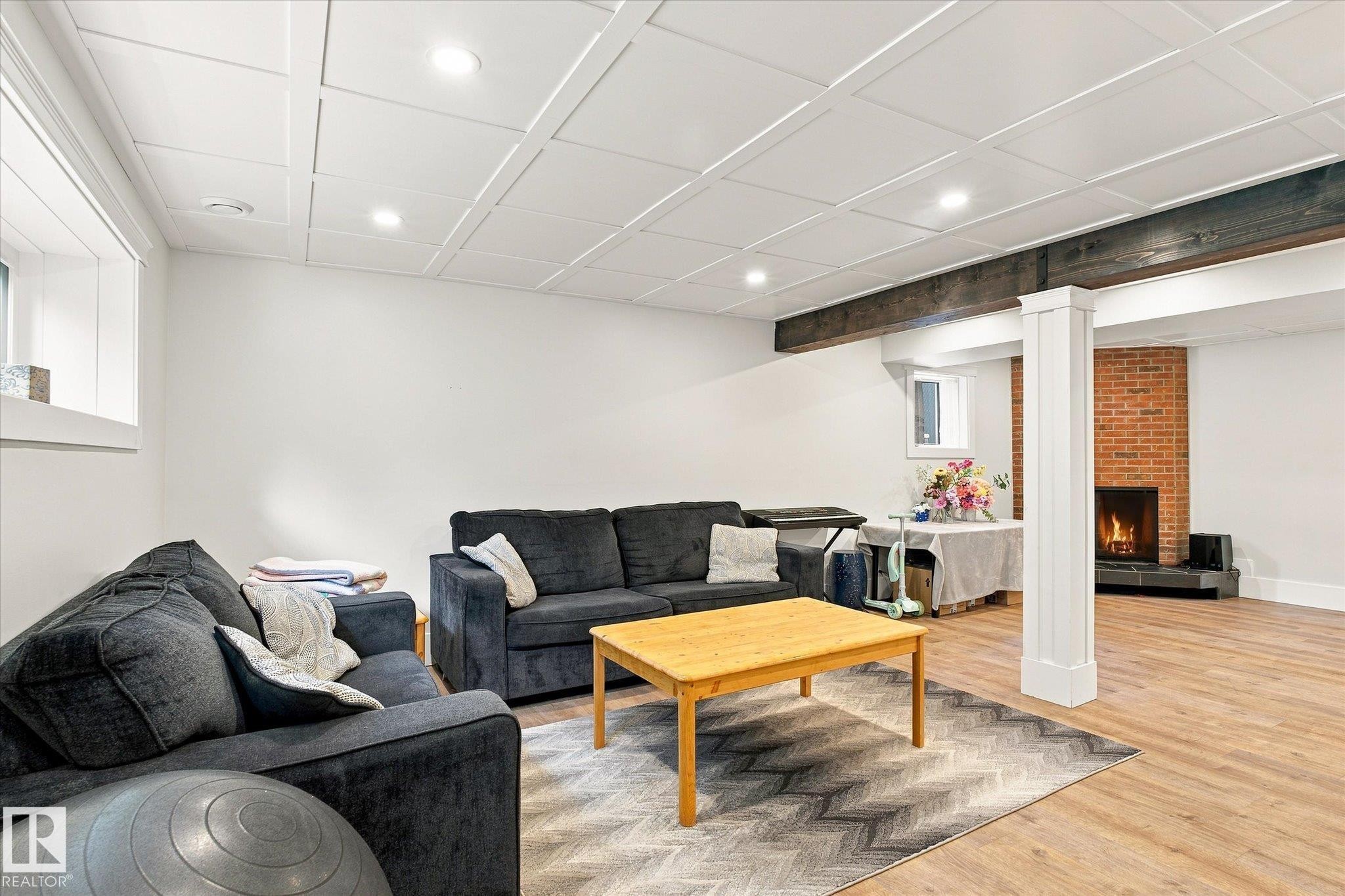 Wood-finish flooring with a fireplace featuring a brick surround, white coffered ceiling, exposed wood beam, and recessed lighting - 3 Akins Drive, St. Albert, AB