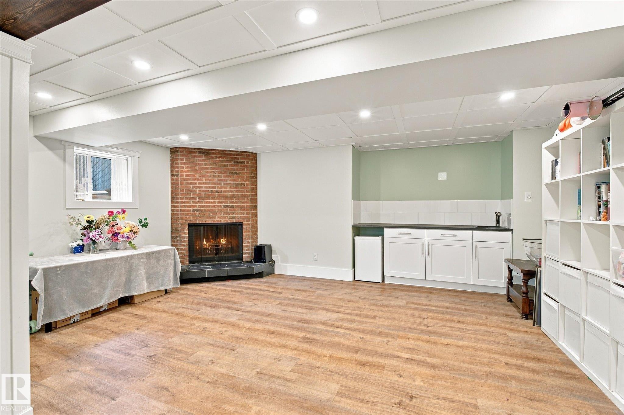 Wood-finish flooring, brick fireplace with a black tile hearth, white paneled ceiling, recessed lighting, and a built-in wet bar with white cabinetry - 3 Akins Drive, St. Albert, AB