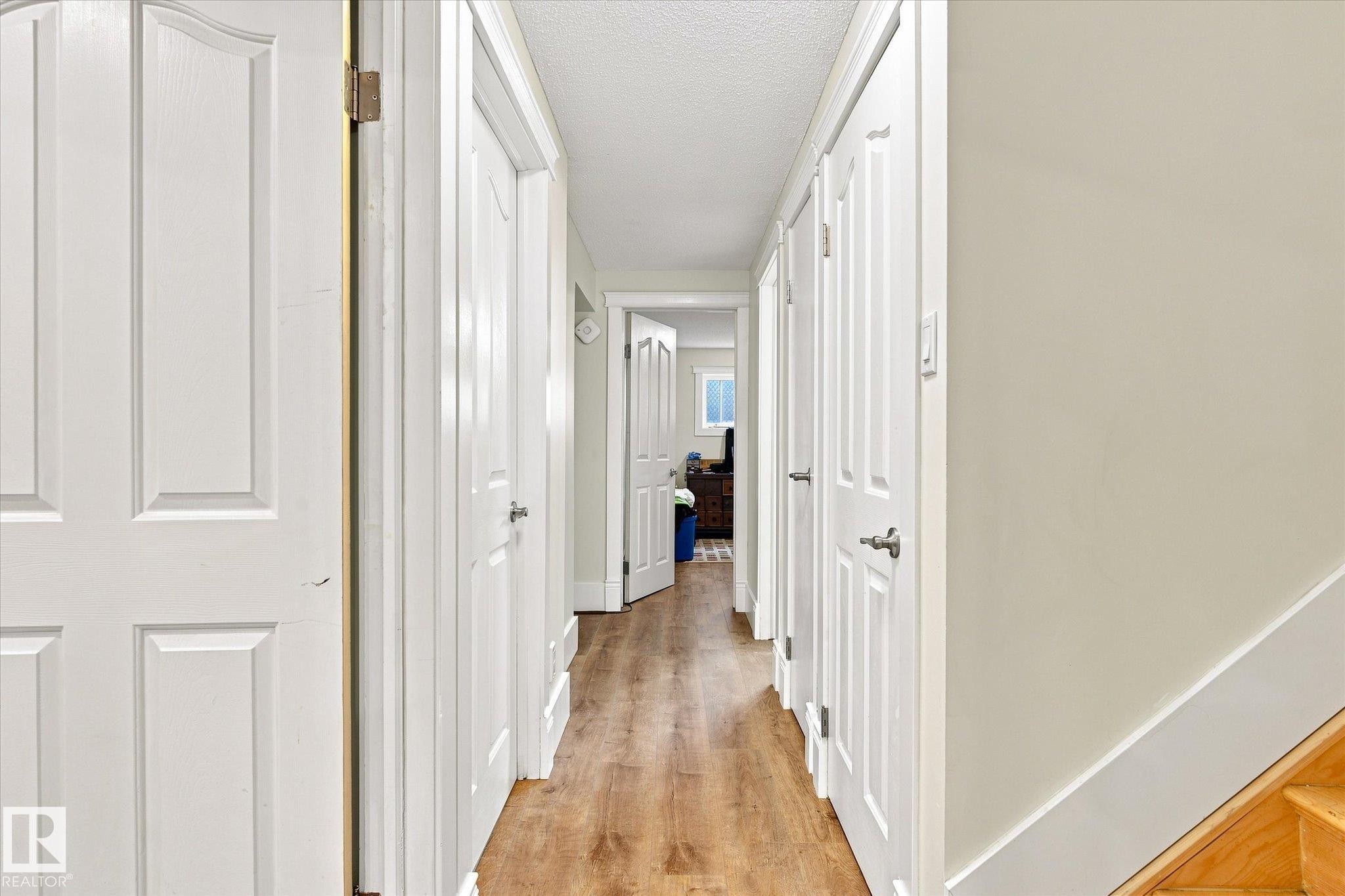 Hallway featuring wood-finish flooring, white panel doors, and neutral painted walls - 3 Akins Drive, St. Albert, AB