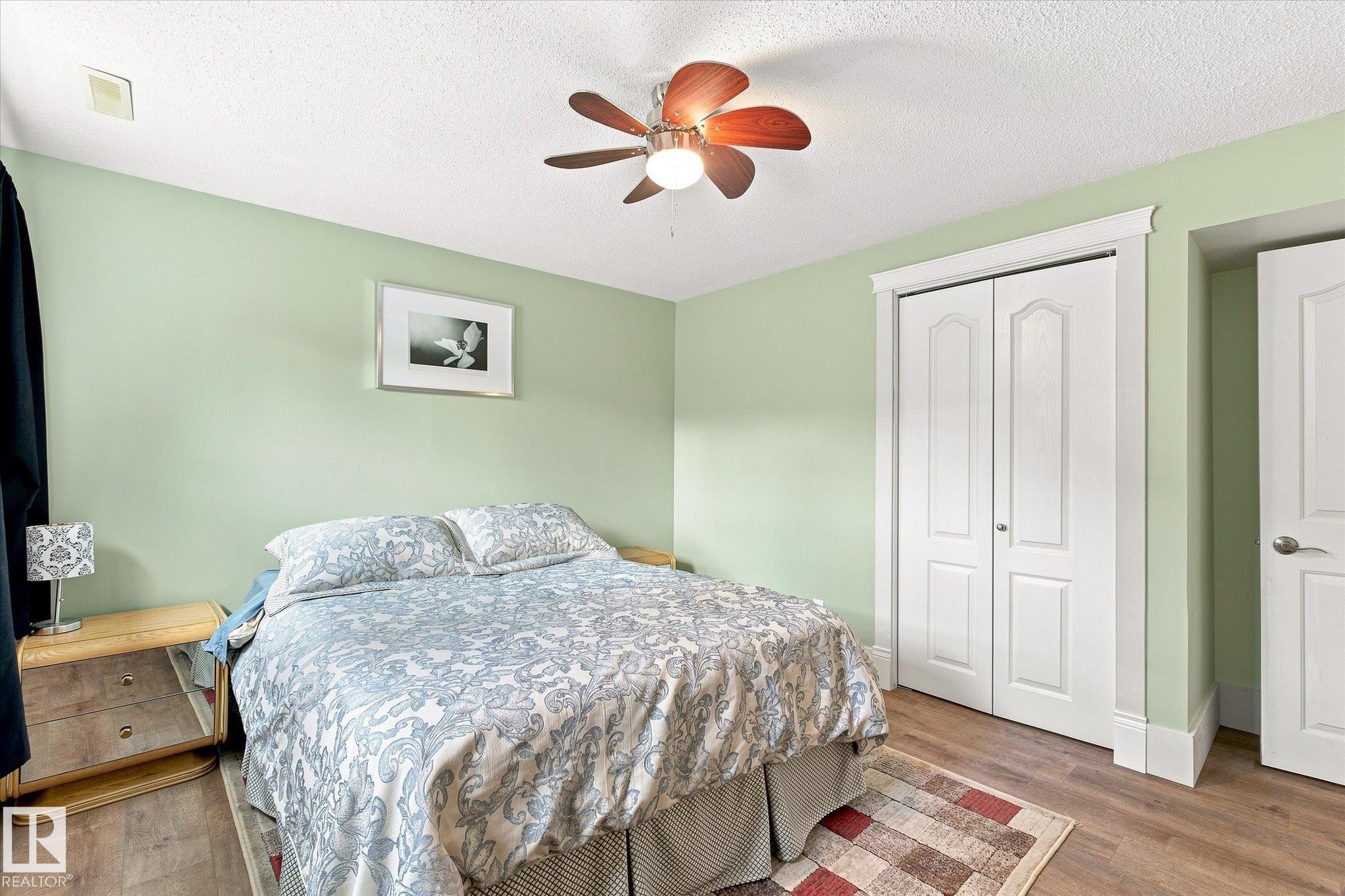 Wood-finish flooring, ceiling fan with light fixture, white bi-fold closet doors, white paneled interior door, and painted walls - 3 Akins Drive, St. Albert, AB