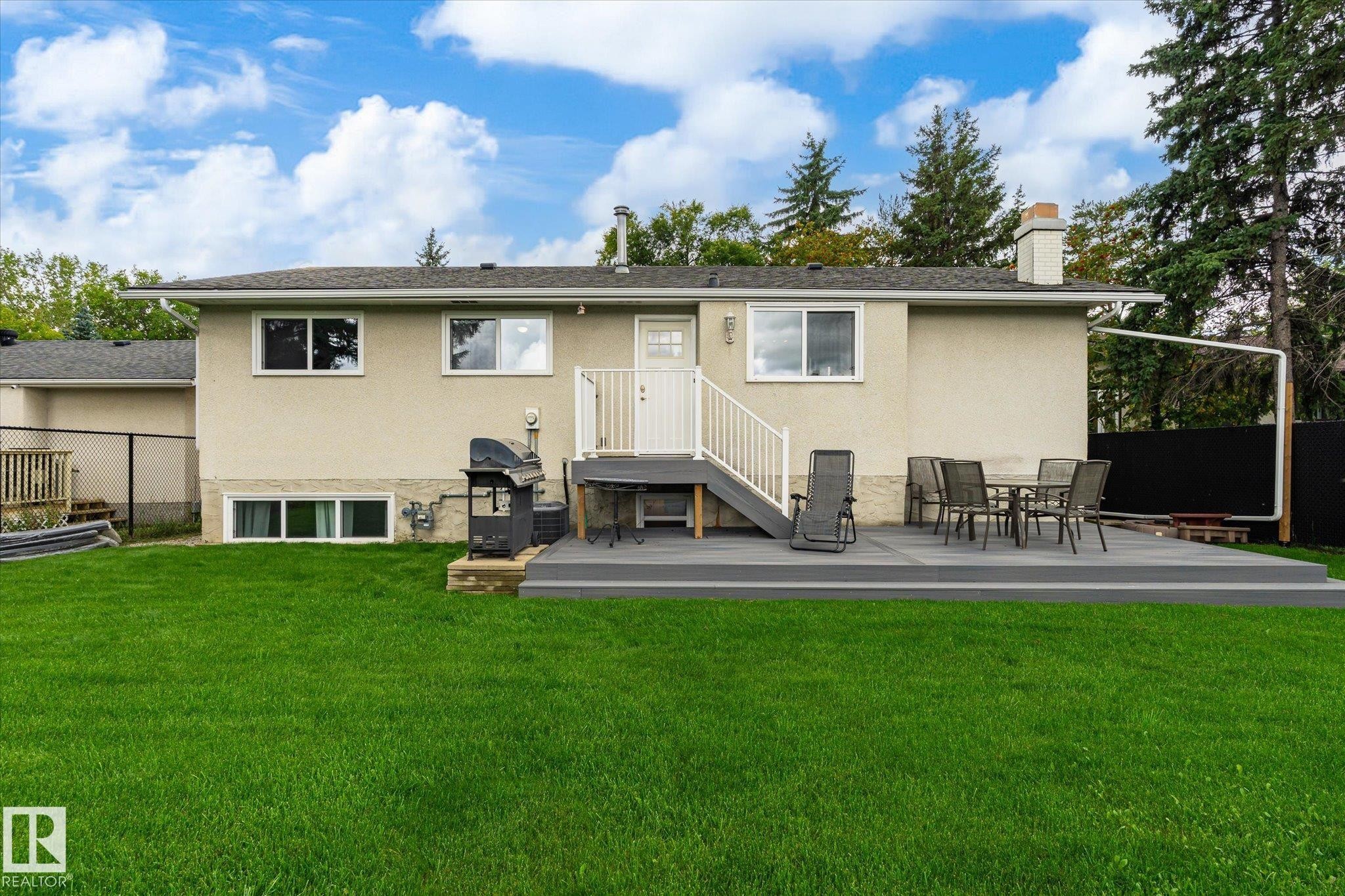 Expansive lawn area with a composite deck, white railing, and stucco exterior - 3 Akins Drive, St. Albert, AB
