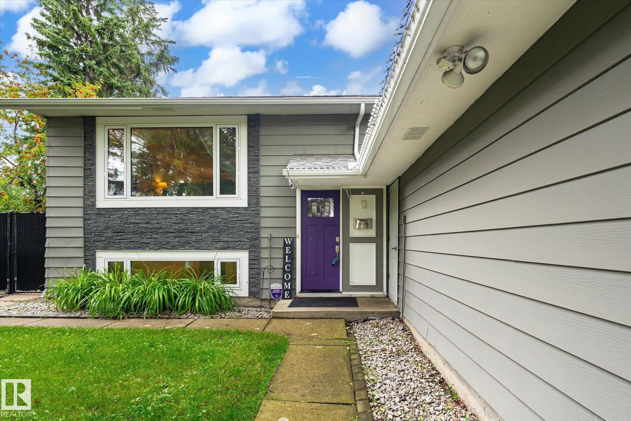 Gray siding exterior with a prominent purple entry door, stone-finish accent paneling, and white-framed windows - 3 Akins Drive, St. Albert, AB
