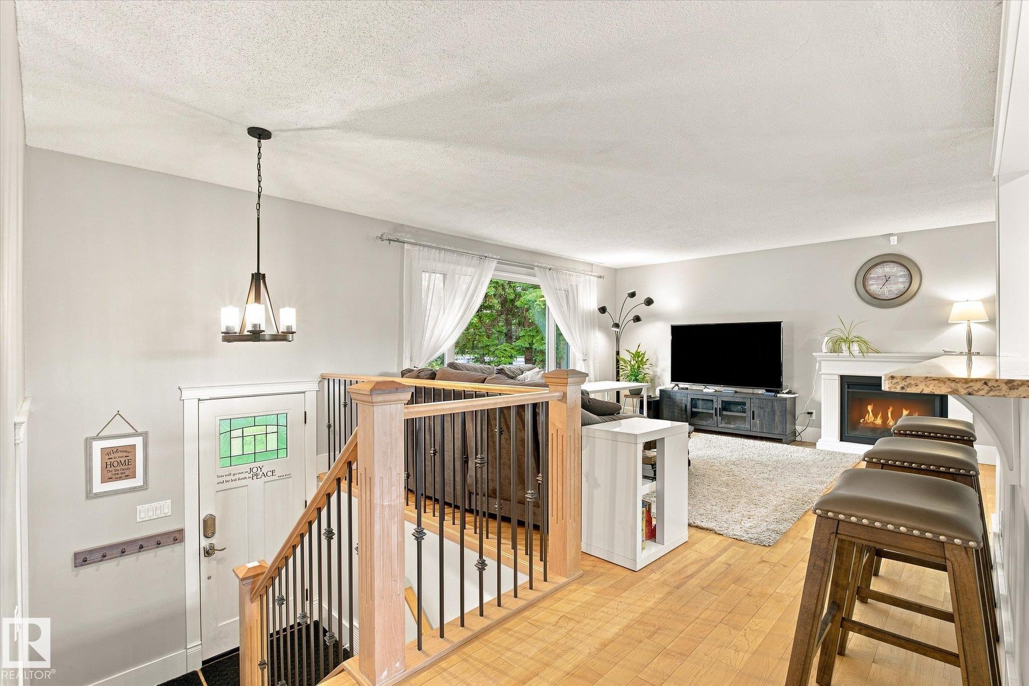 Hardwood flooring, wrought iron stair balusters, wood railing, electric fireplace with mantel, and a multi-light pendant fixture - 3 Akins Drive, St. Albert, AB