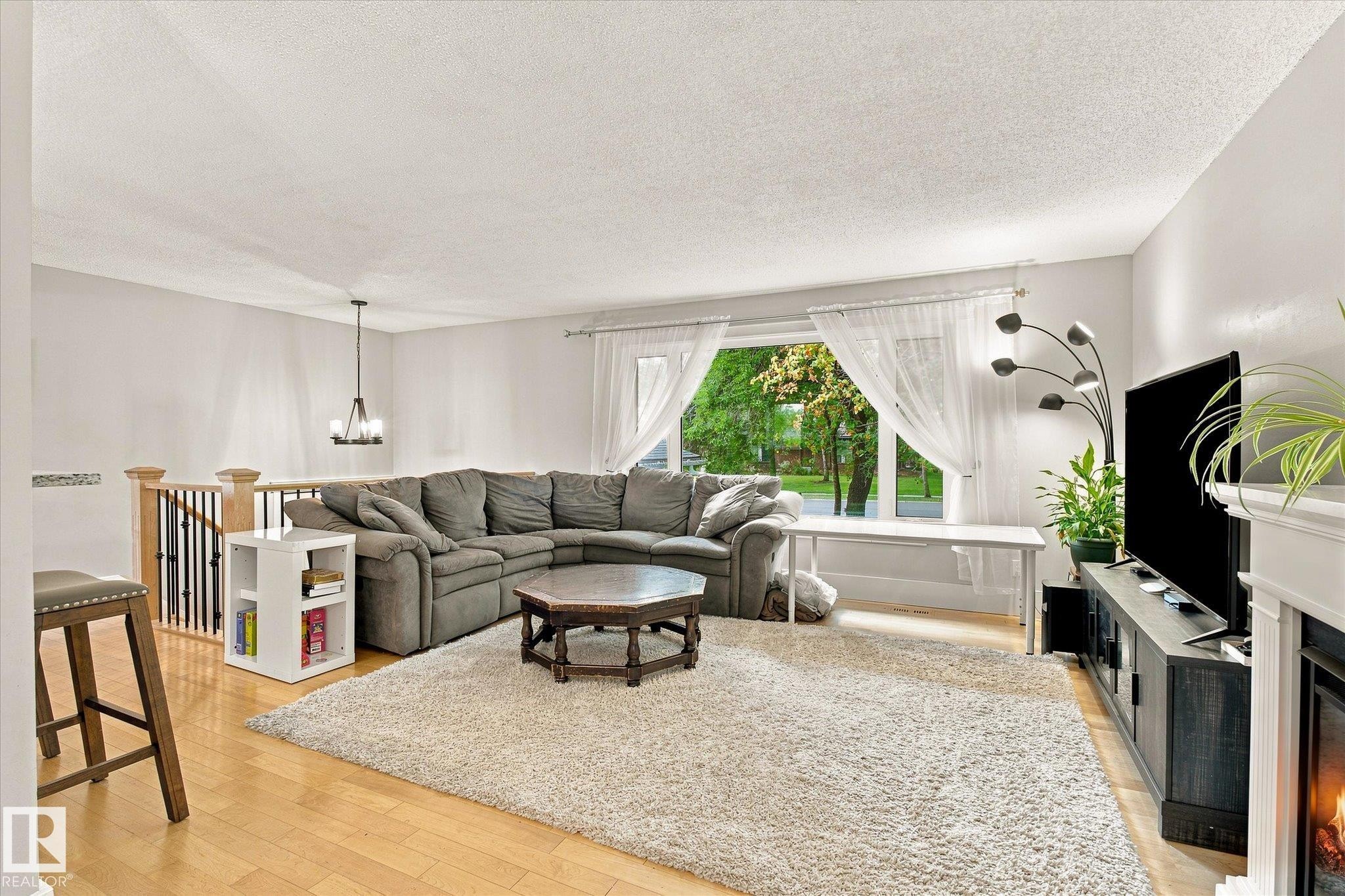Hardwood-style flooring, white walls, built-in fireplace, and a contemporary chandelier - 3 Akins Drive, St. Albert, AB