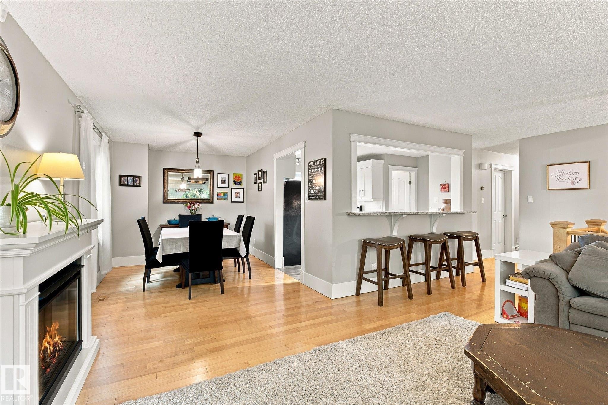 Wood-finish flooring throughout, a built-in fireplace with a white mantel, and a dining area with a contemporary pendant light fixture - 3 Akins Drive, St. Albert, AB