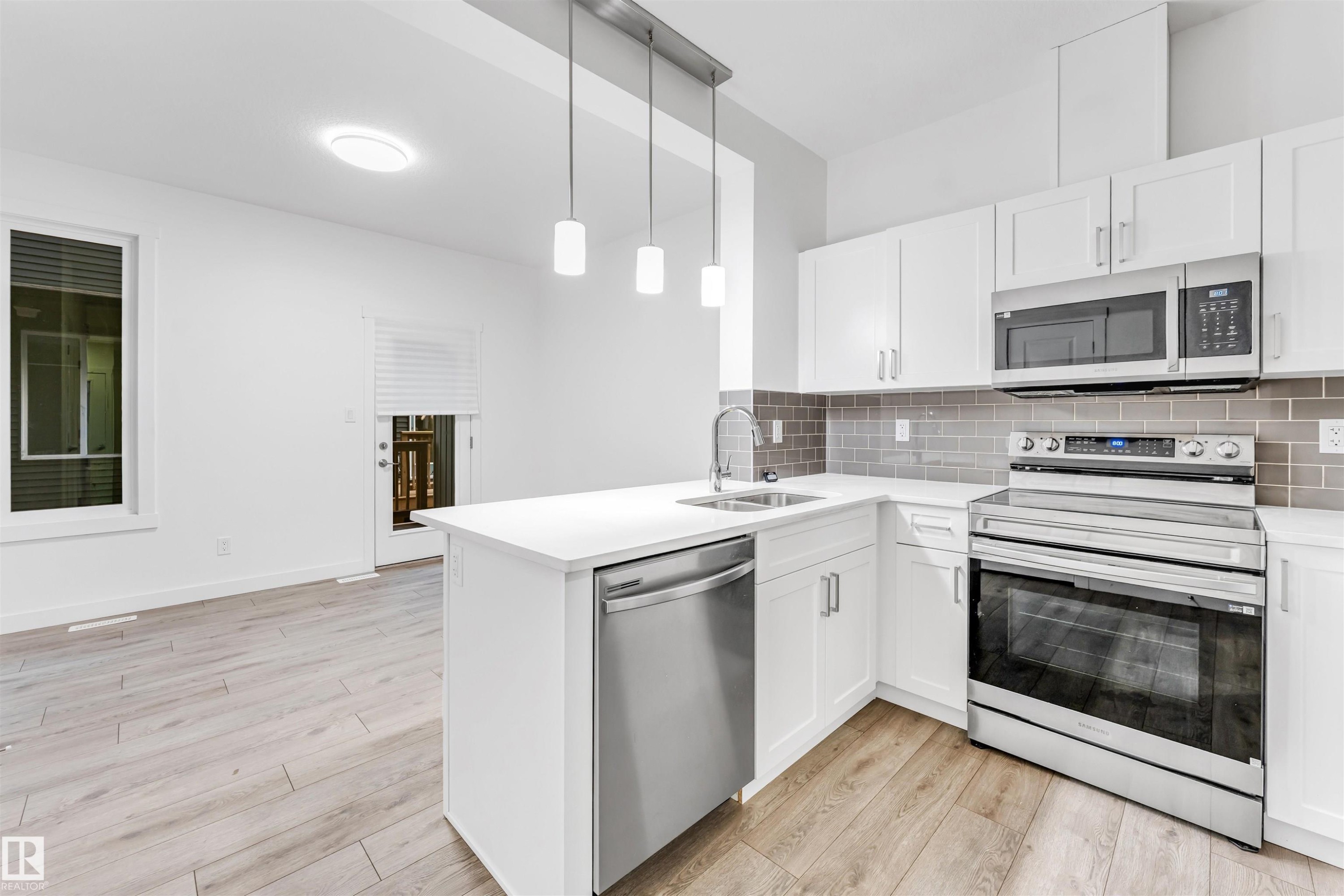Kitchen featuring white cabinetry, stainless steel appliances, a white island, grey subway tile backsplash, and wood-finish flooring - #45 2710 66 St Sw, Edmonton, AB