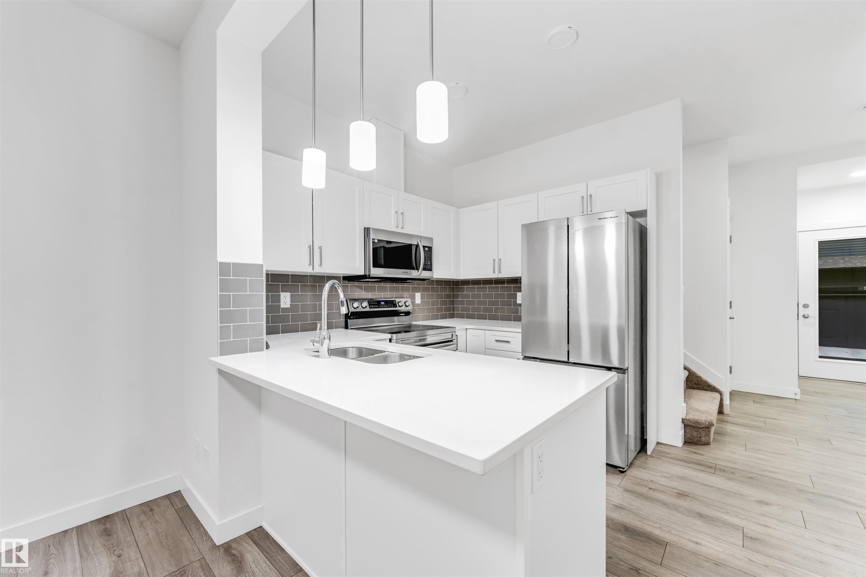 Kitchen featuring white cabinetry, stainless steel appliances, a subway tile backsplash, and light wood-finish flooring - #45 2710 66 St Sw, Edmonton, AB