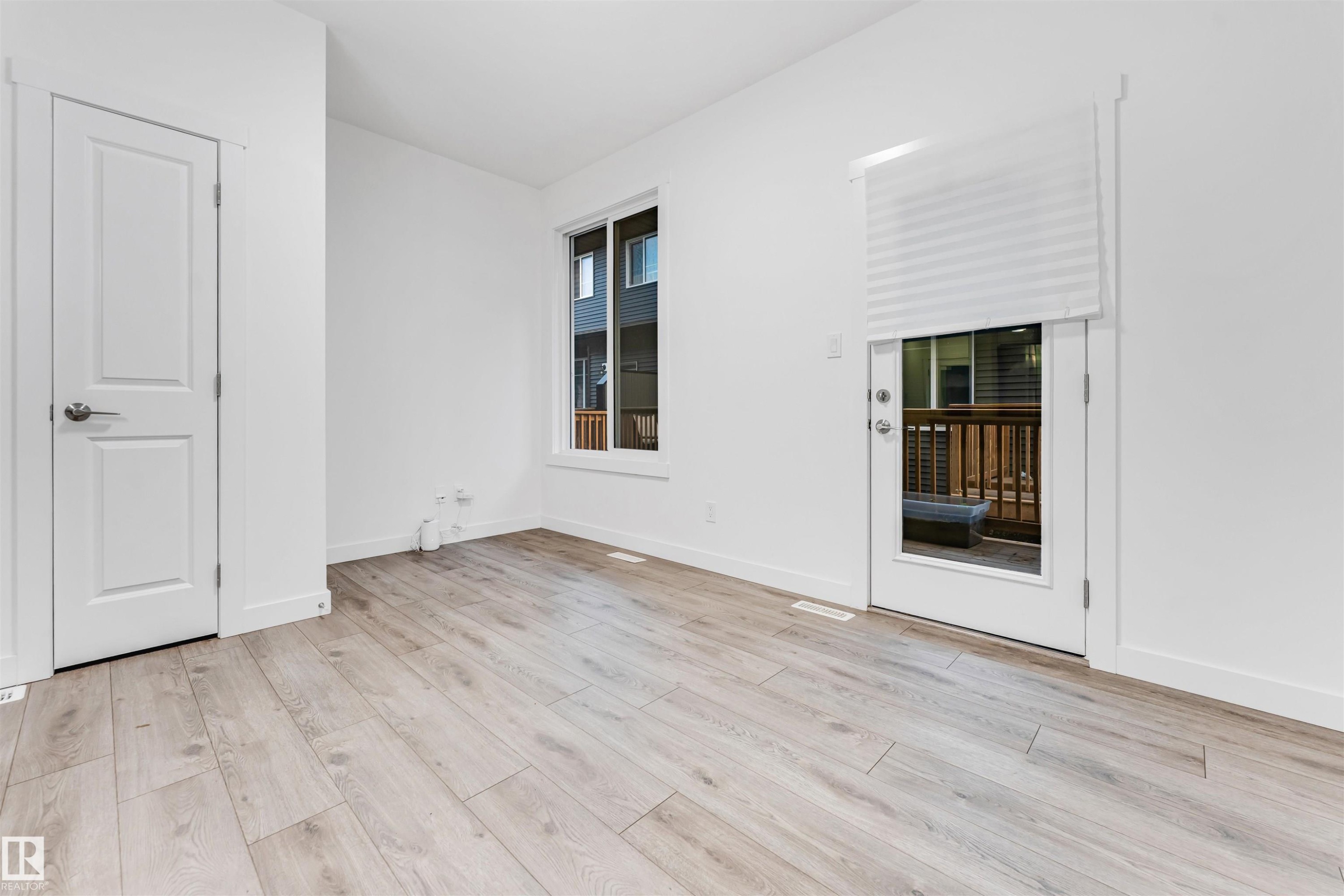Wood-finish flooring, white walls, white trim, white two-panel door, and a glass-paneled exterior door - #45 2710 66 St Sw, Edmonton, AB