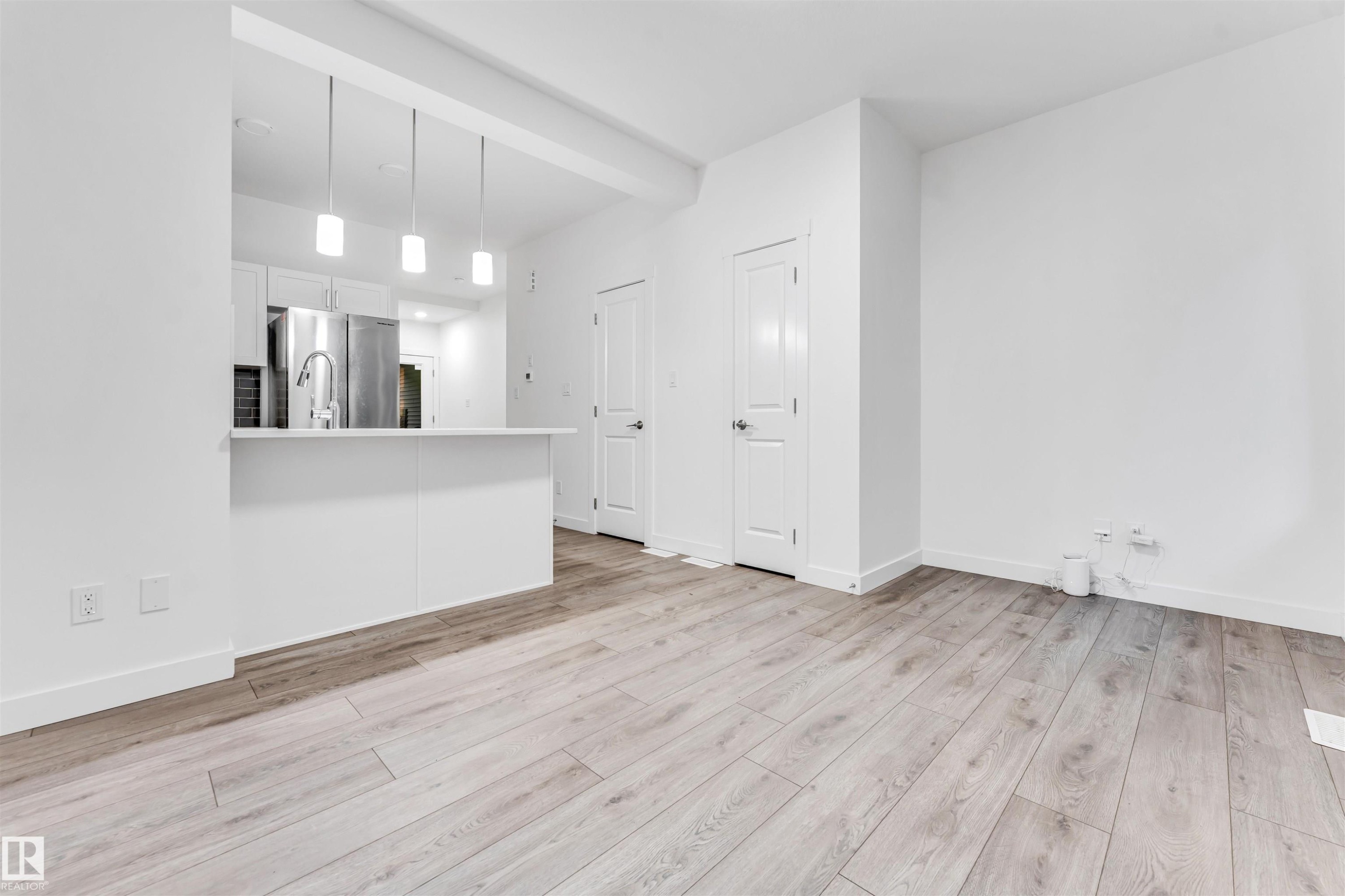 Wood-finish flooring throughout, stainless steel appliances, white kitchen cabinetry, kitchen island with seating, and pendant lighting - #45 2710 66 St Sw, Edmonton, AB