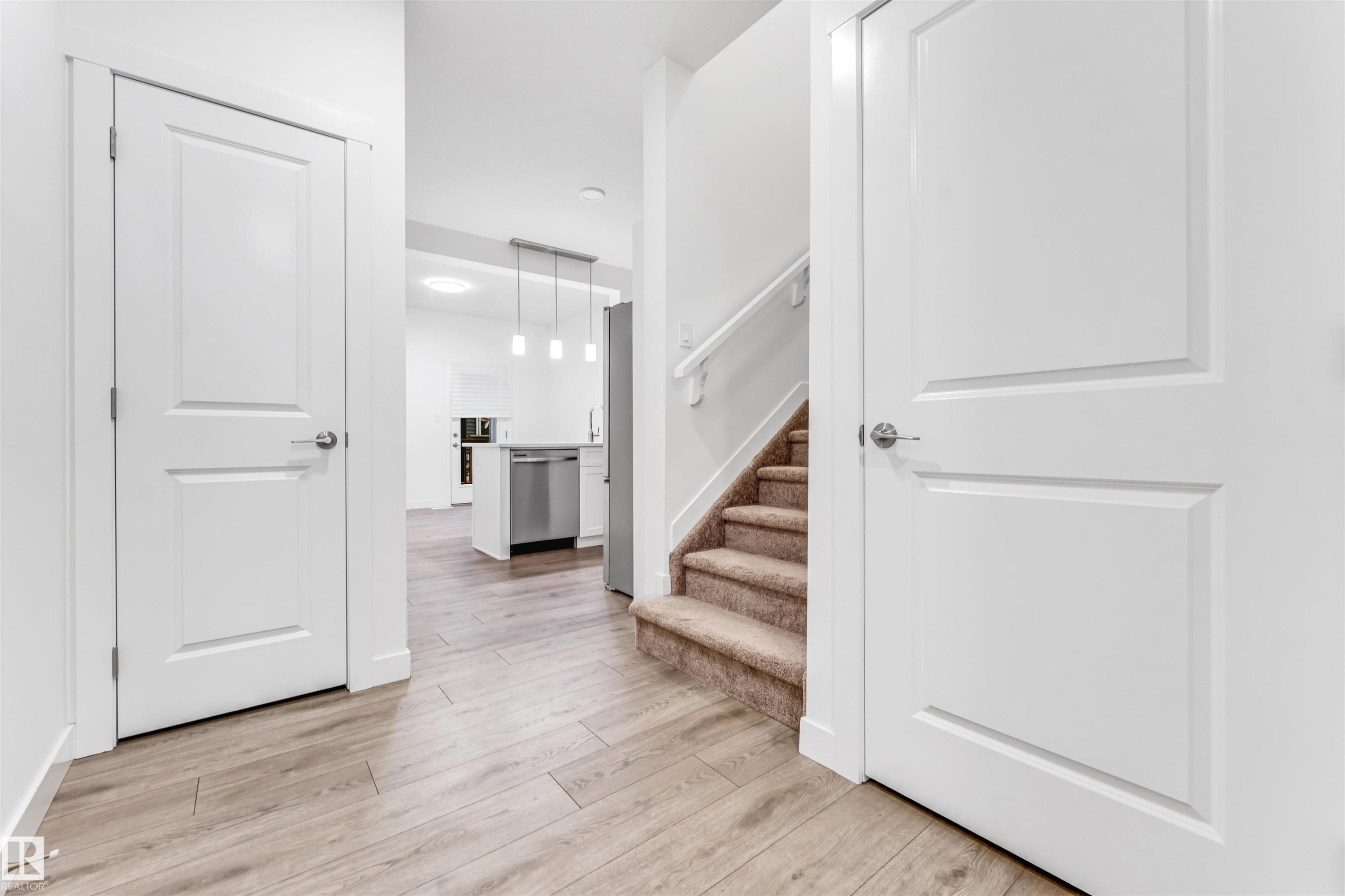 Warm wood-finish flooring, white paneled doors, and a carpeted staircase with a white handrail - #45 2710 66 St Sw, Edmonton, AB