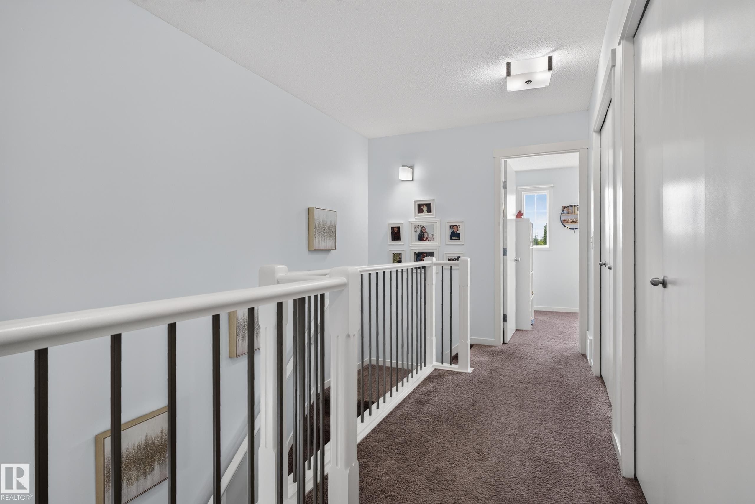 Upper landing featuring white painted balusters and black metal spindles, textured carpeting, and white doors with dark hardware - 17363 120 Street Nw, Edmonton, AB