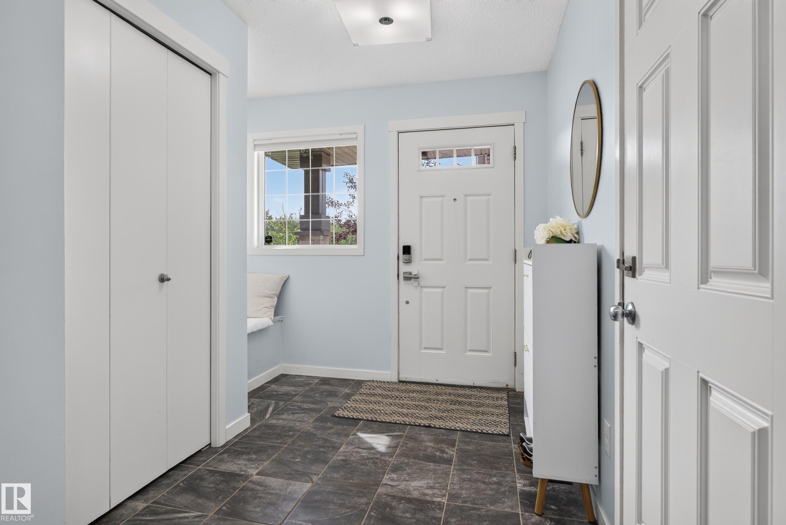 Entryway featuring dark tile flooring, a built-in window bench, a white paneled entry door with transom lites, and bi-fold closet doors - 17363 120 Street Nw, Edmonton, AB