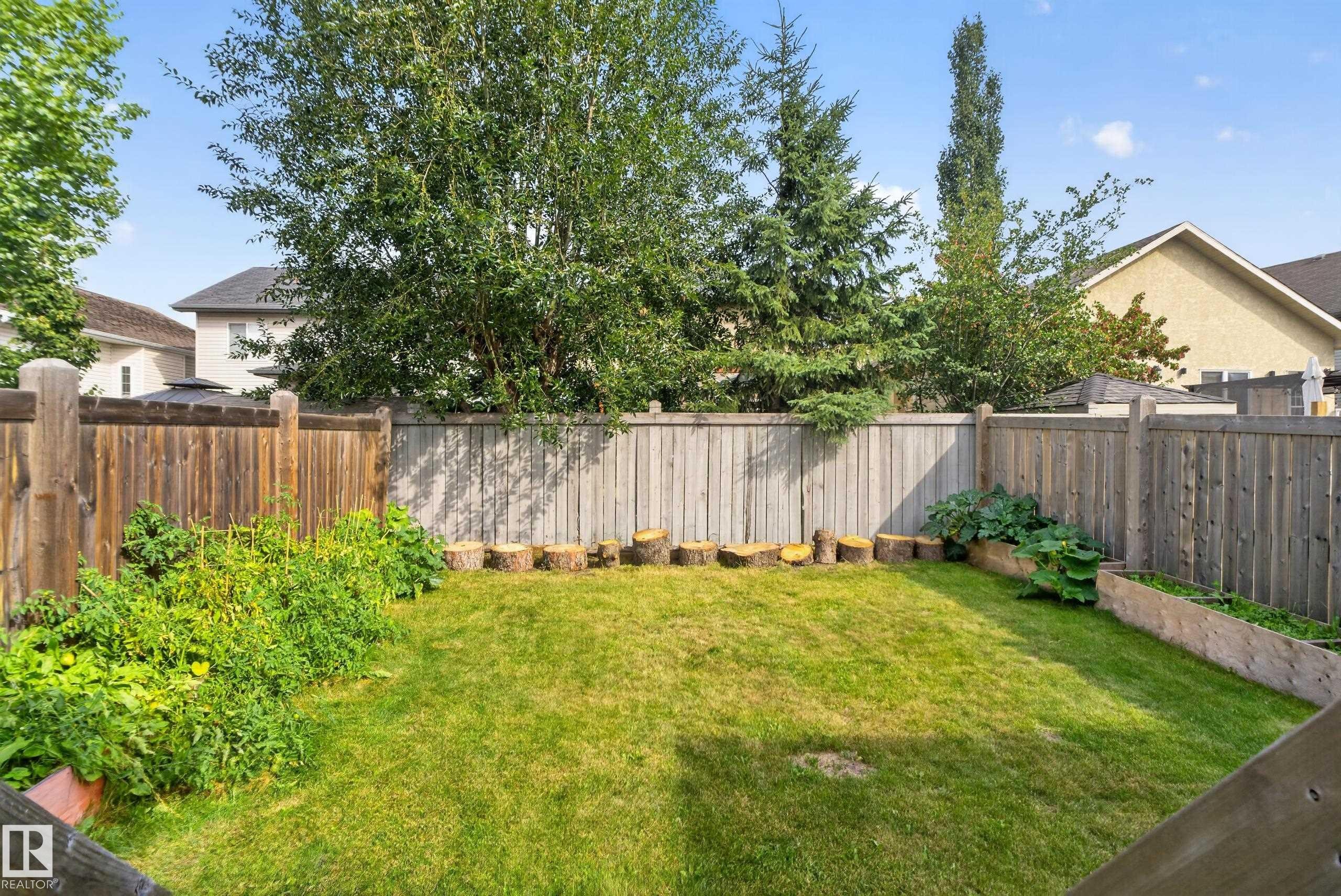 Fenced backyard featuring a manicured lawn, established garden beds, and mature perimeter trees - 17363 120 Street Nw, Edmonton, AB