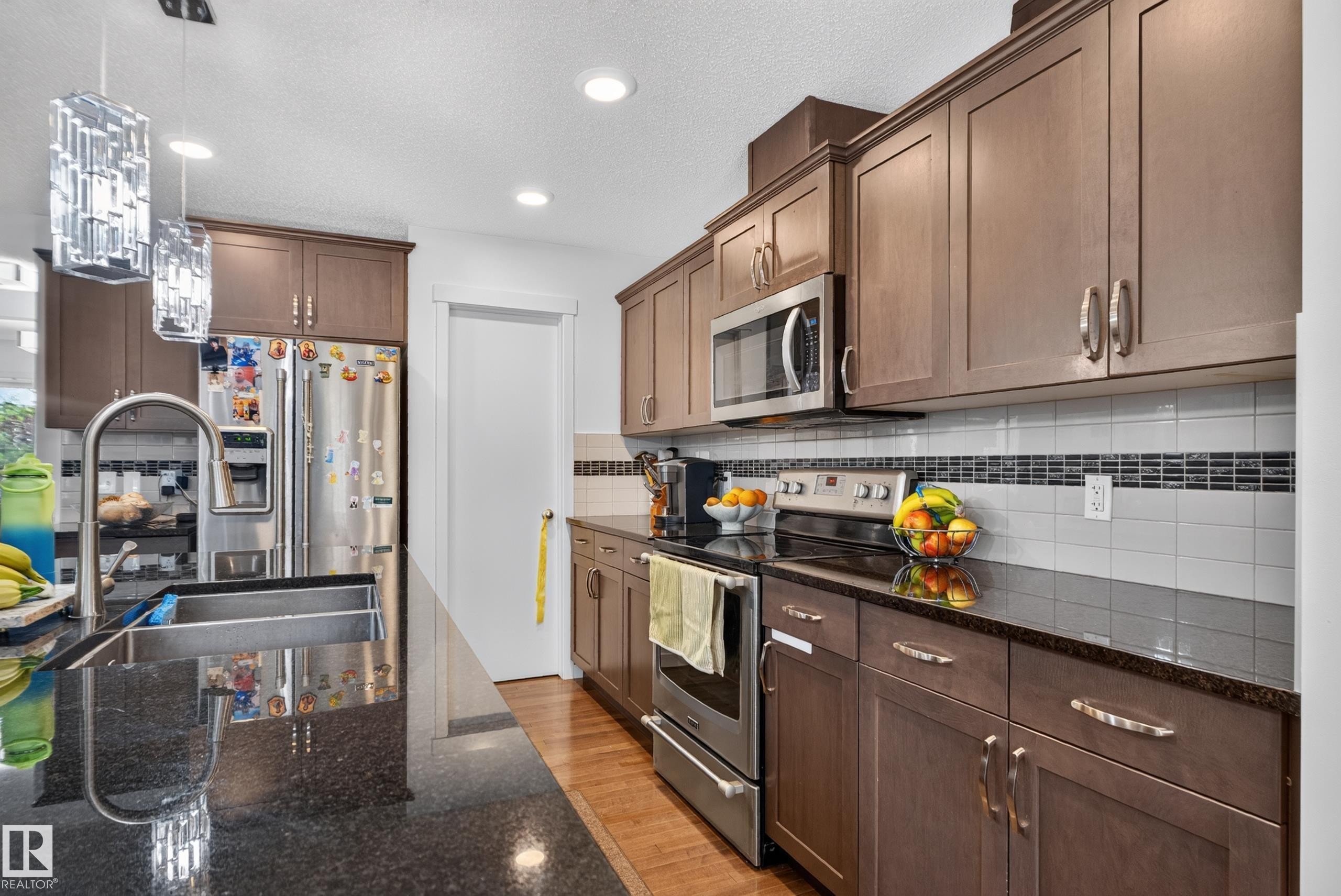 Kitchen featuring wood-finish cabinetry, stainless steel appliances, dark stone countertops, tile backsplash with decorative accent, and recessed lighting - 17363 120 Street Nw, Edmonton, AB