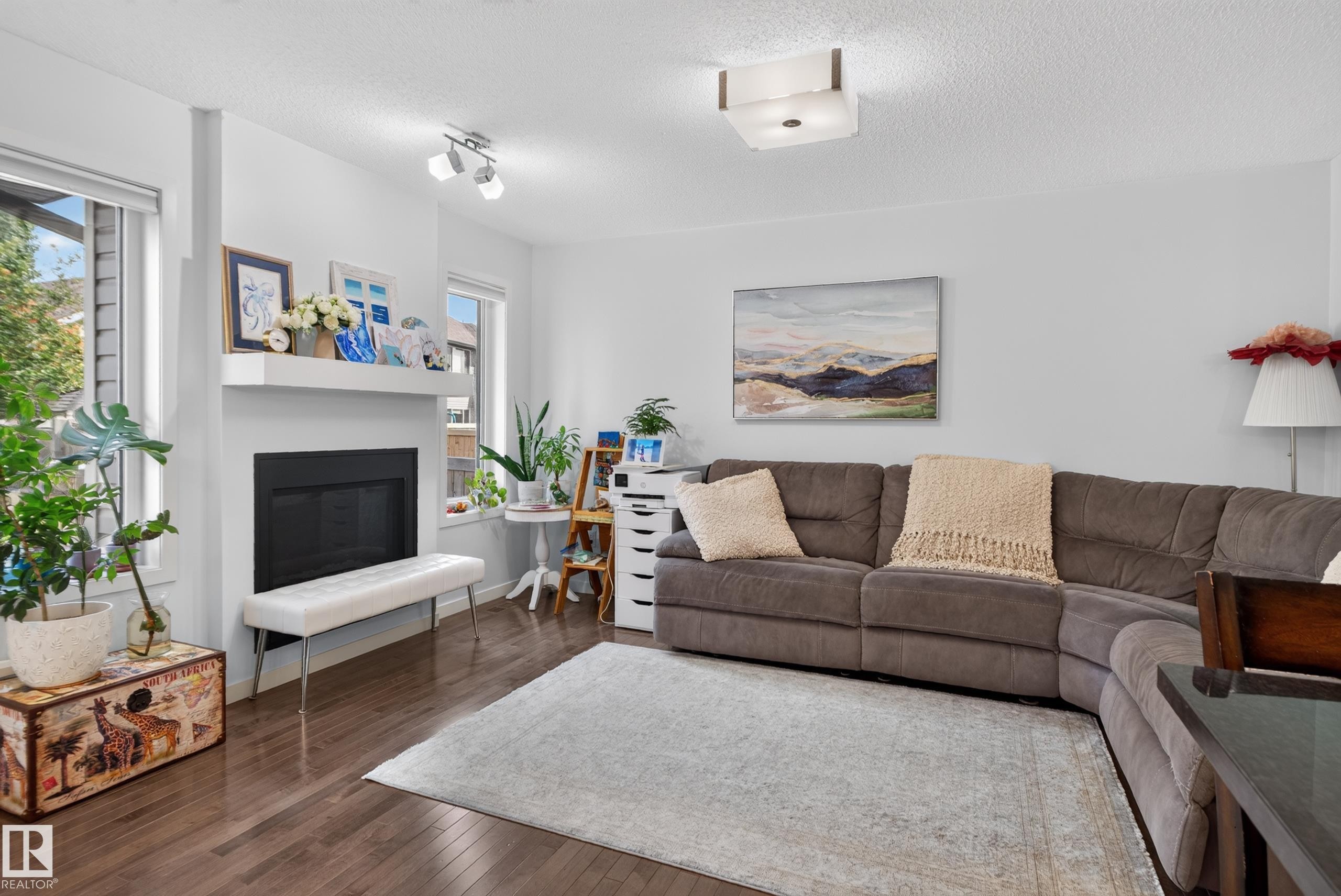 Wood-finish flooring, white walls, multiple windows, a built-in fireplace with a mantel, and a flush-mount ceiling light - 17363 120 Street Nw, Edmonton, AB