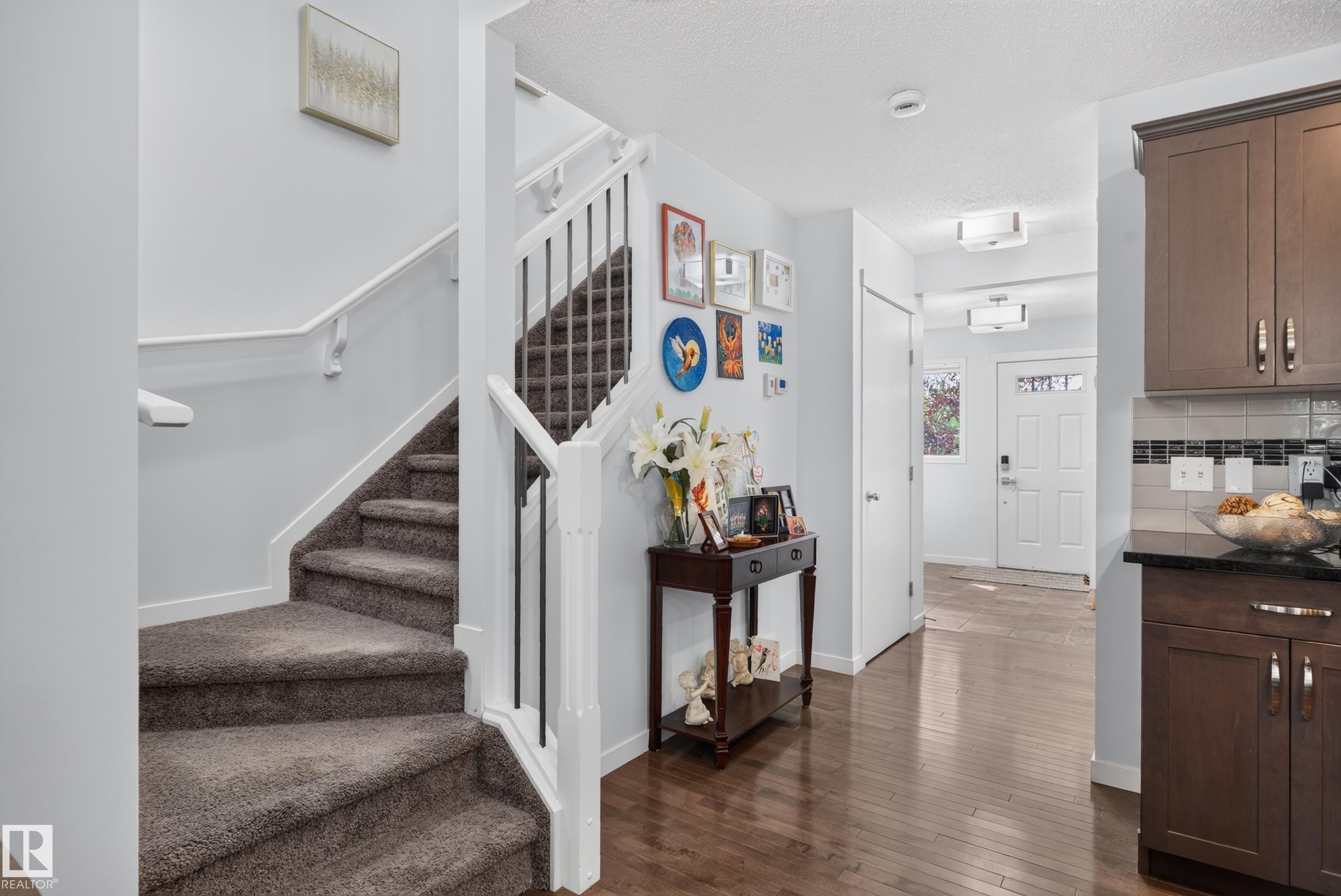 Carpeted staircase with white risers and railings, wood-finish flooring, white paneled interior doors, dark wood-finish cabinetry, and black countertop - 17363 120 Street Nw, Edmonton, AB