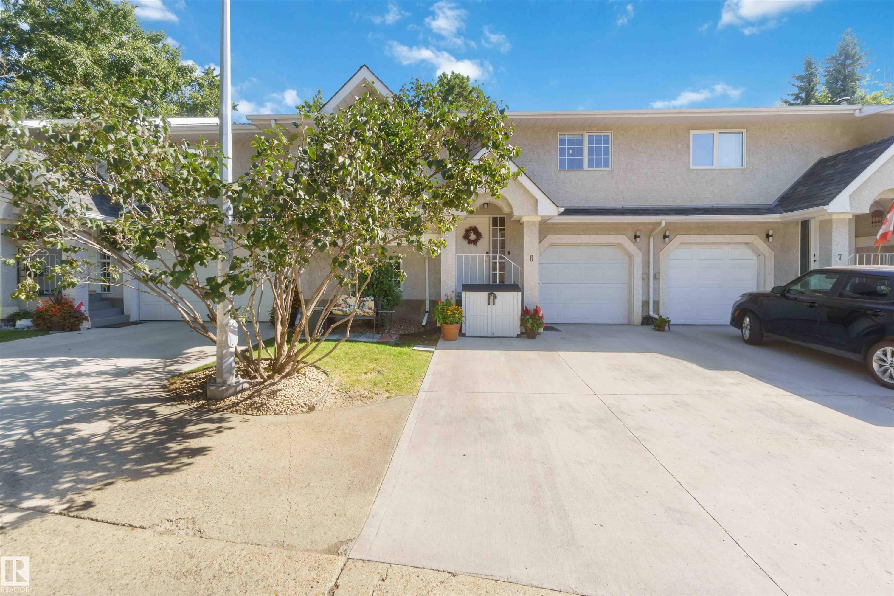 Stucco exterior with multiple dormer windows, a concrete driveway, two single-car garages, and mature landscaping - #6 15 Poirier Av, St. Albert, AB