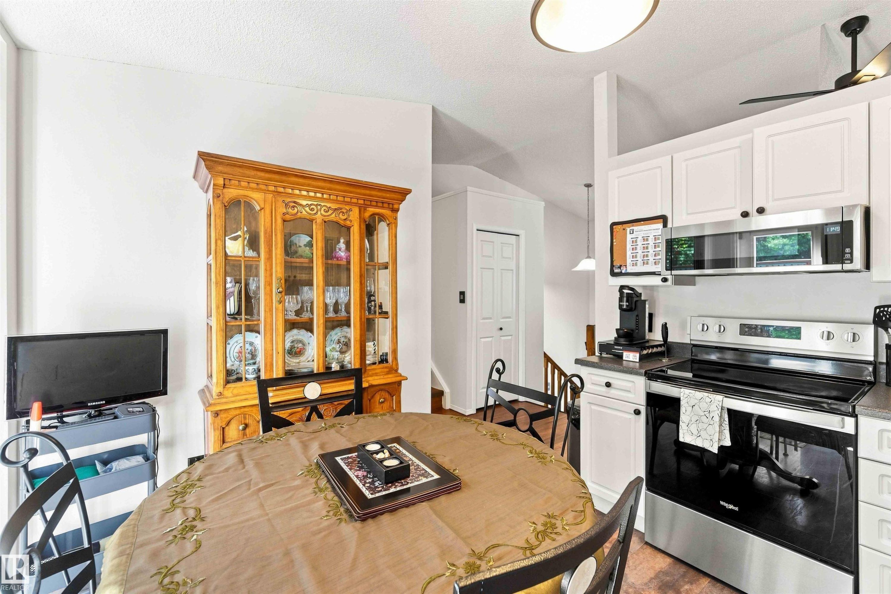 White cabinetry with dark hardware, stainless steel range, stainless steel microwave, stone-finish countertops, and wood-finish flooring - #6 15 Poirier Av, St. Albert, AB