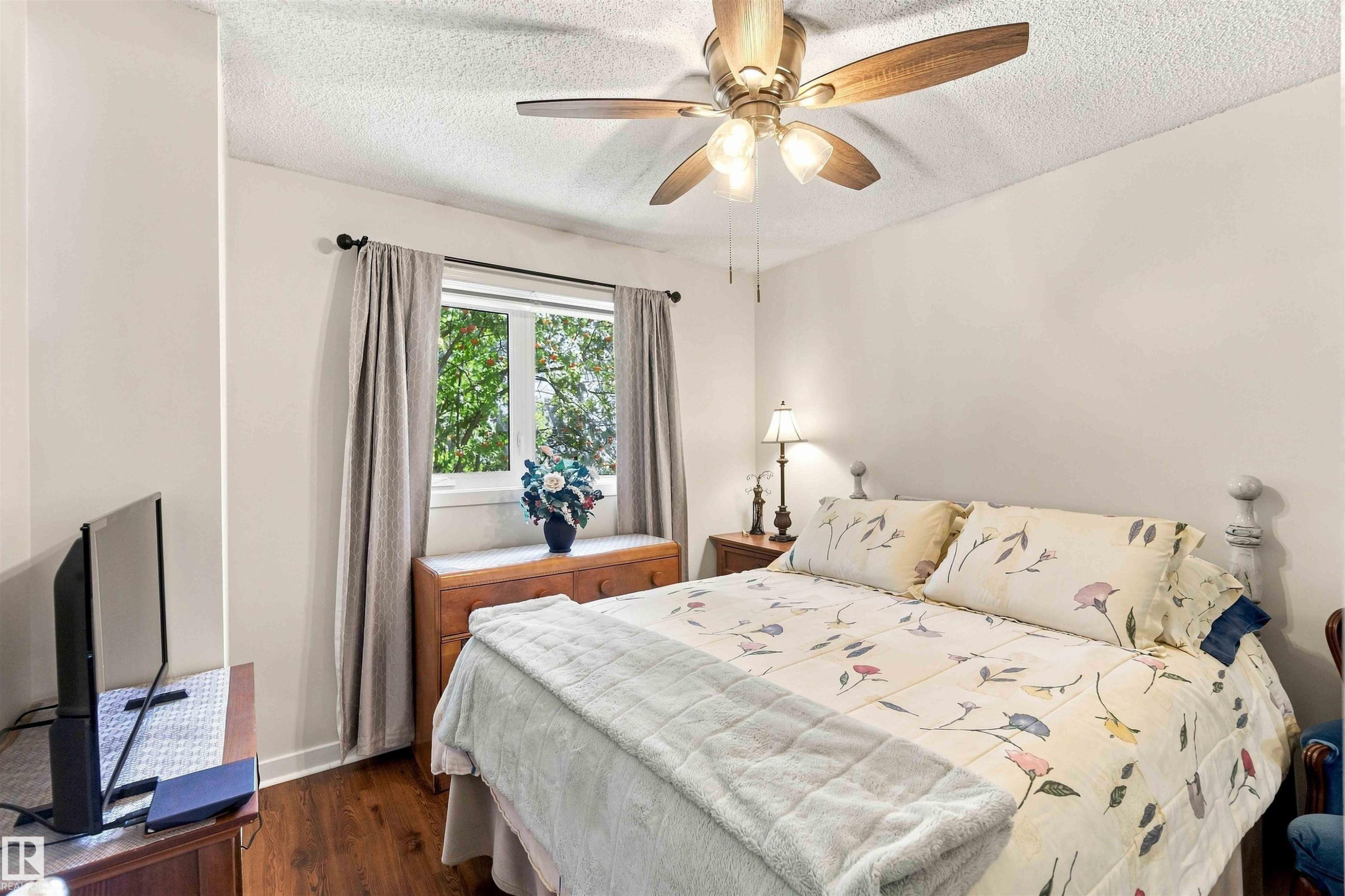 Wood-finish flooring, ceiling fan with light fixture, window with curtains, and neutral wall paint - #6 15 Poirier Av, St. Albert, AB