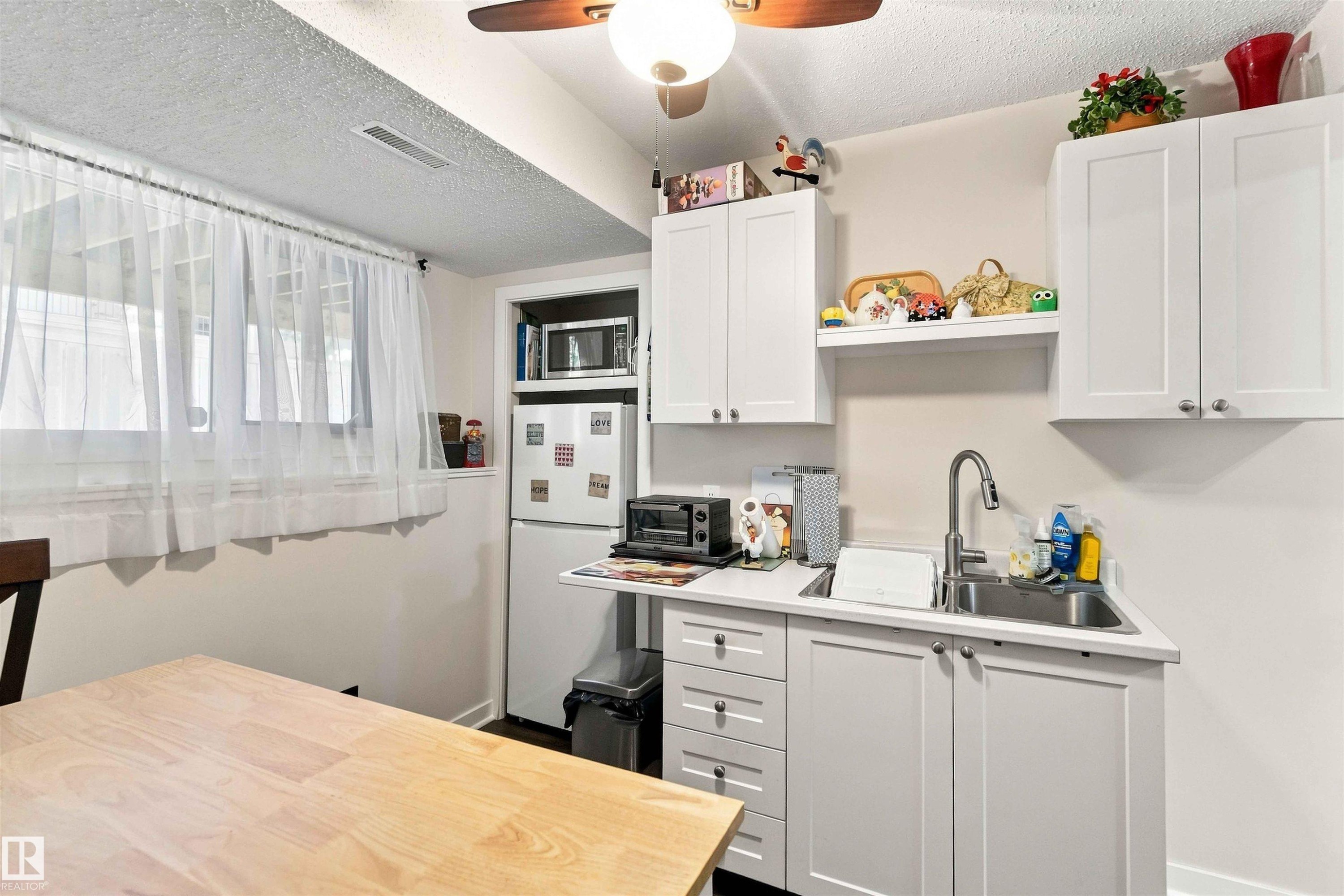 White cabinetry with silver hardware, stainless steel sink with gooseneck faucet, light-toned countertop, and recessed refrigerator space - #6 15 Poirier Av, St. Albert, AB