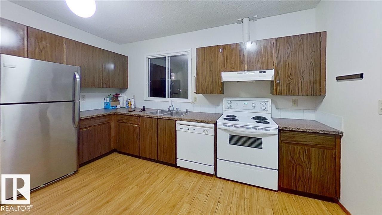 Kitchen featuring wood-finish cabinetry, light tone flooring, stainless steel refrigerator, white range, and white dishwasher - 4611 52 Avenue, Stony Plain, AB