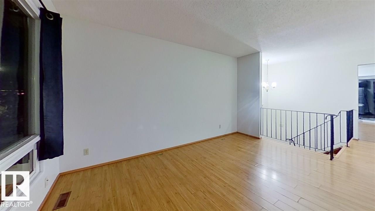 Expansive space featuring wood-finish flooring, a large window, a metal railing, and a chandelier - 4611 52 Avenue, Stony Plain, AB