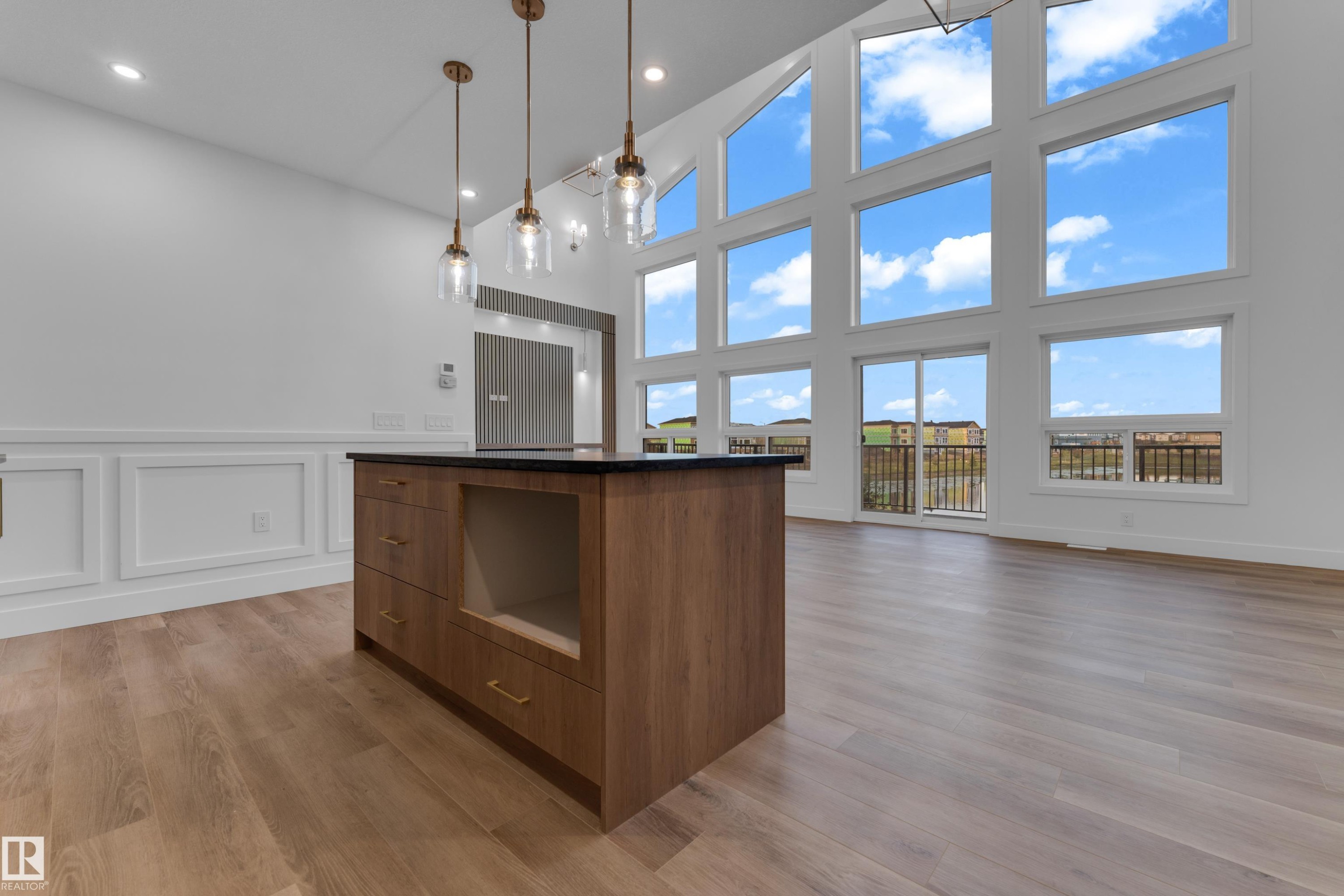Vaulted ceilings with expansive window arrays, wood-finish flooring, a kitchen island with dark countertop, and decorative wall paneling - 236 Linden Loop, Leduc, AB