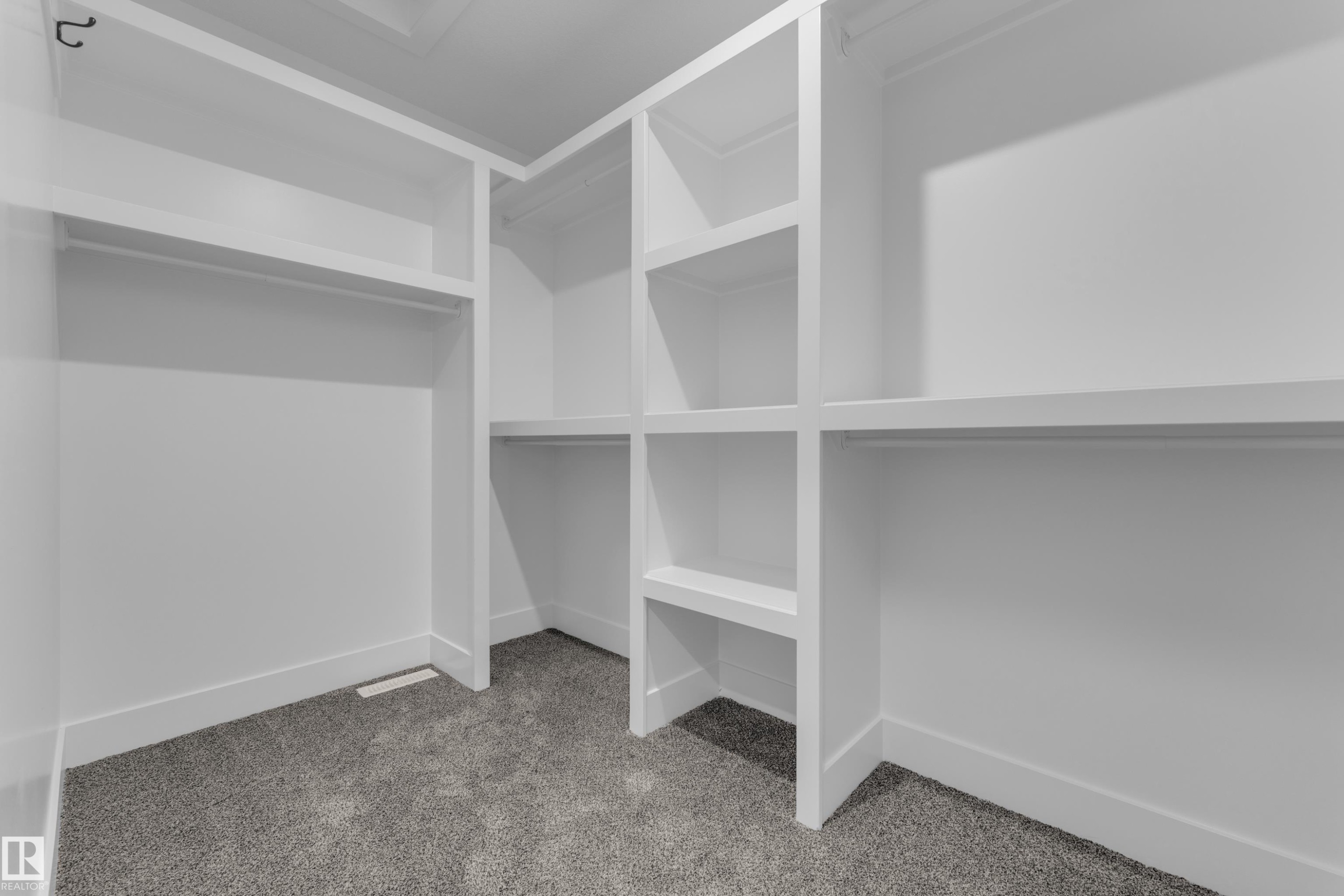 Built-in shelving with multiple storage compartments, integrated hanging rods, white finish, and gray carpeting - 236 Linden Loop, Leduc, AB