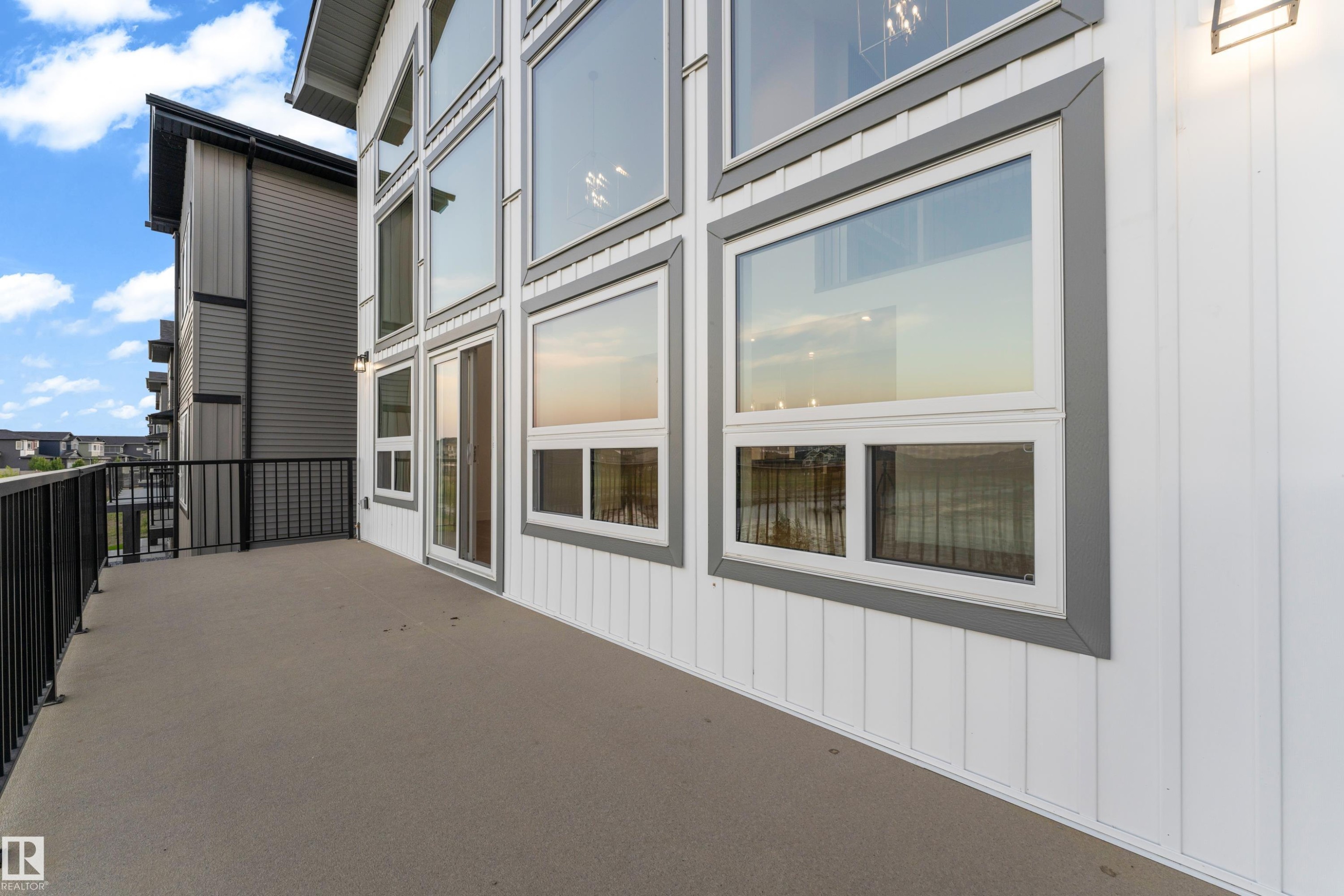 Modern exterior featuring expansive multi-pane windows with aluminum framing, horizontal corrugated metal siding accents, and a spacious concrete deck with metal railings overlooking the surrounding landscape - 236 Linden Loop, Leduc, AB