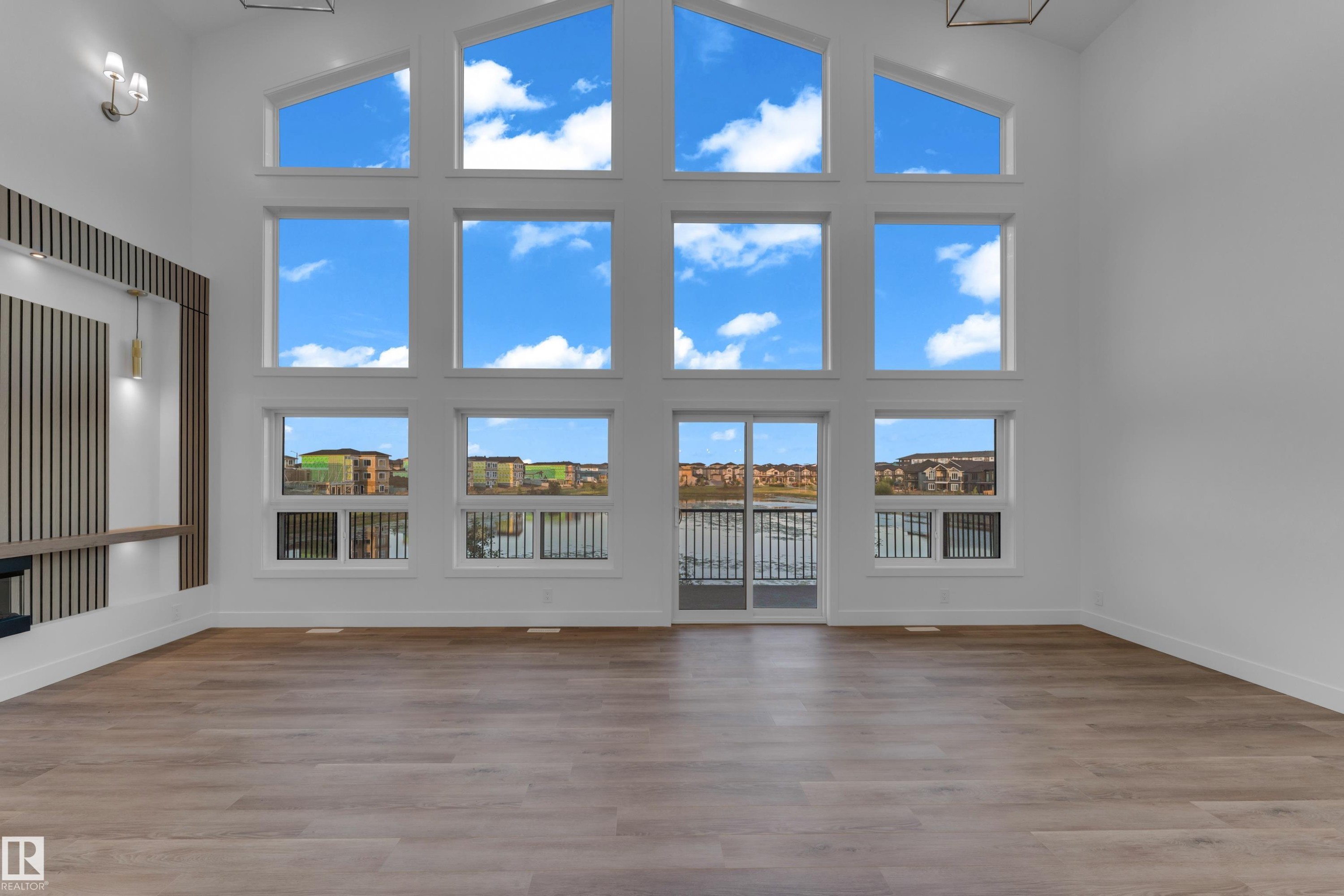 Expansive living area with high ceilings, large windows, wood-finish flooring, and contemporary wall sconces - 236 Linden Loop, Leduc, AB