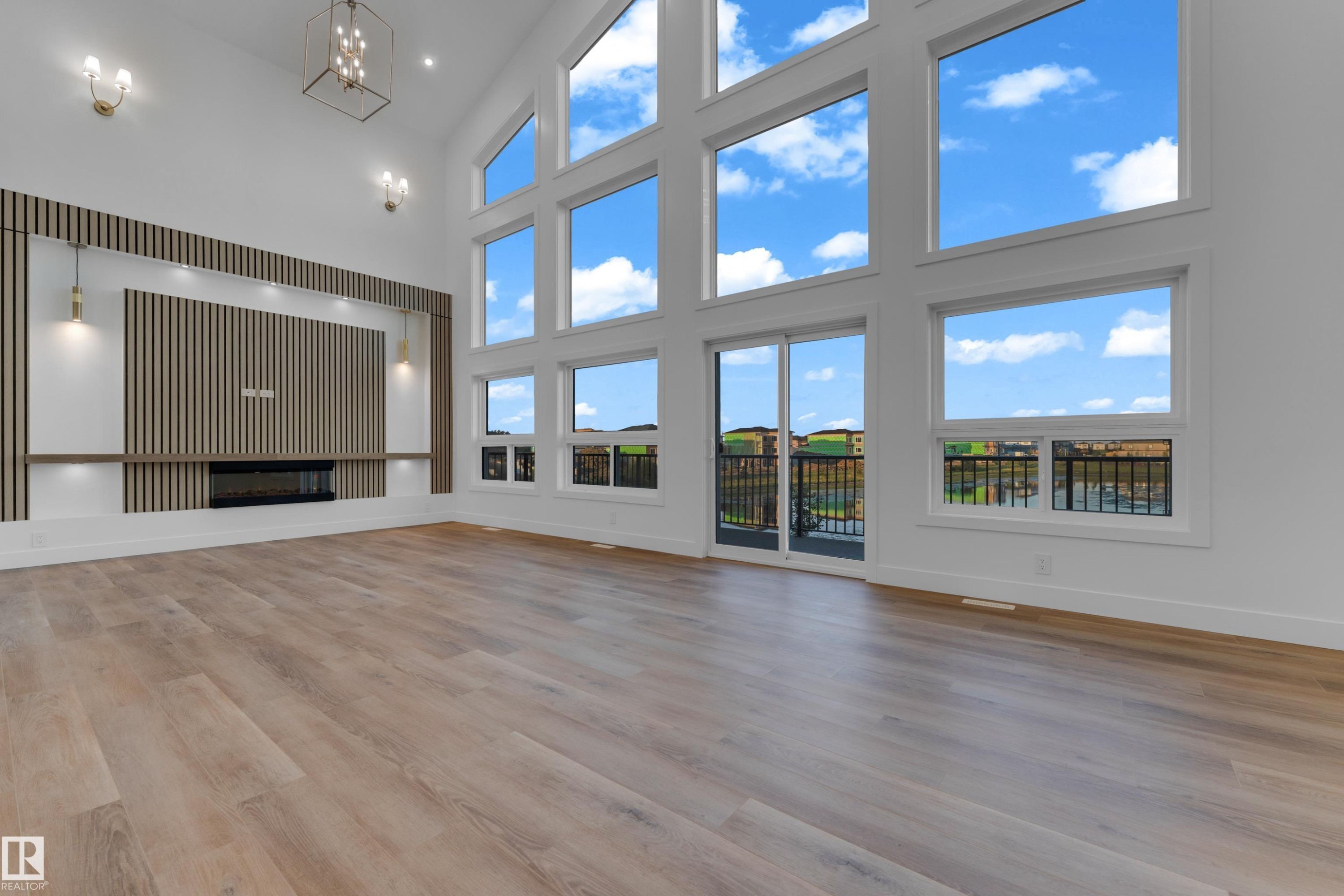 Vaulted ceiling with a contemporary chandelier, wood-finish flooring, built-in fireplace, and expansive windows - 236 Linden Loop, Leduc, AB