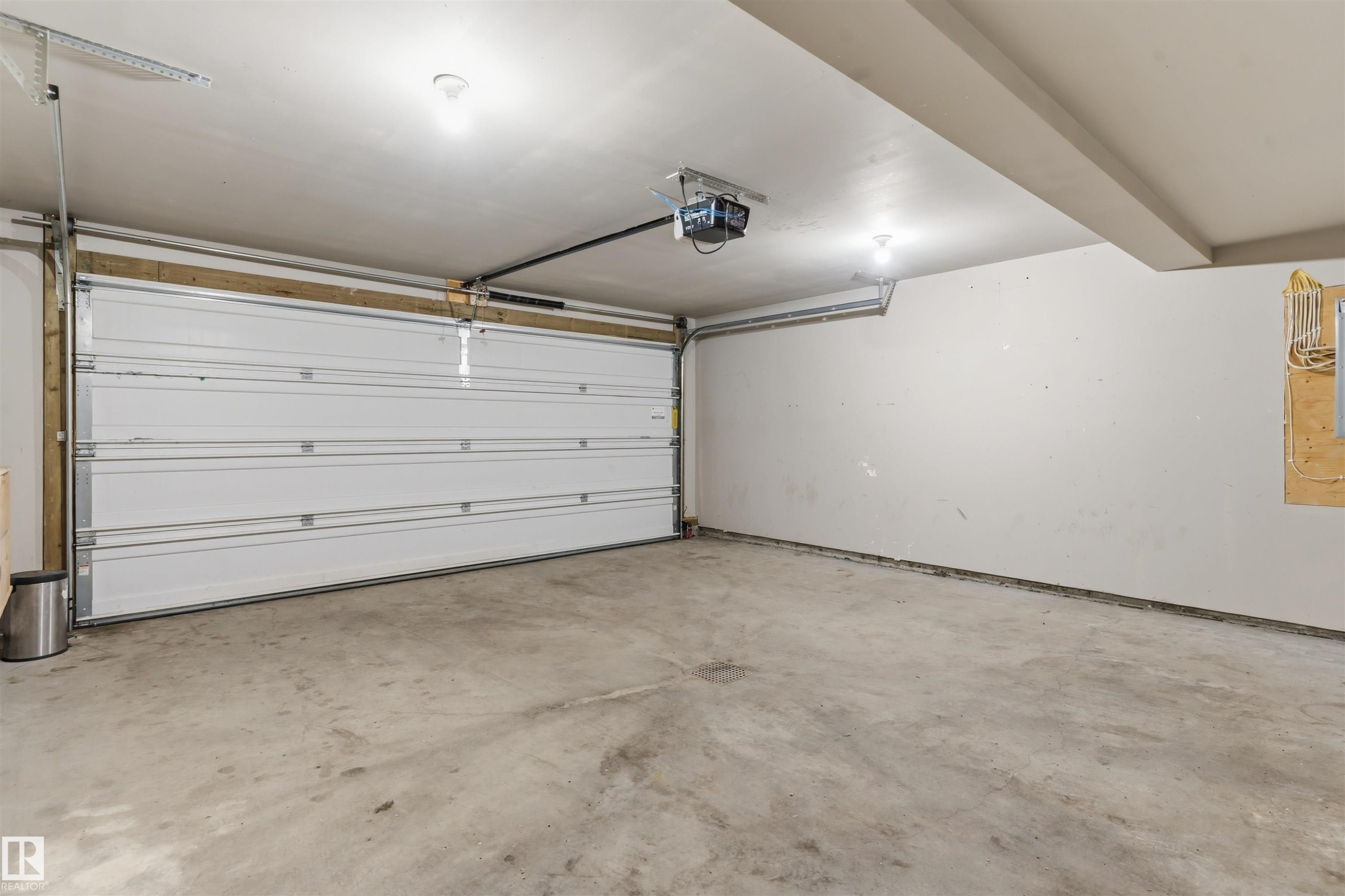 Attached garage with a white sectional door, concrete flooring, and ceiling-mounted lighting - #62 675 Watt Bv Sw, Edmonton, AB