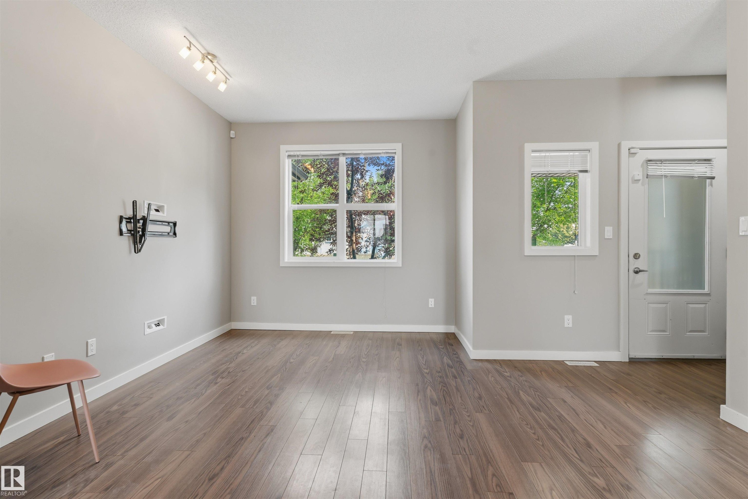 Wood-finish flooring, neutral wall tones, multiple windows, track lighting, and a glass-panel door - #62 675 Watt Bv Sw, Edmonton, AB