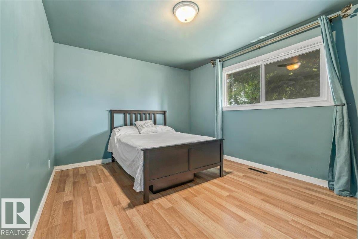 Spacious room featuring wood-finish flooring, light blue walls, and a large window with white trim - 13320 123 Street Nw, Edmonton, AB - Indoor Photo Showing Bedroom