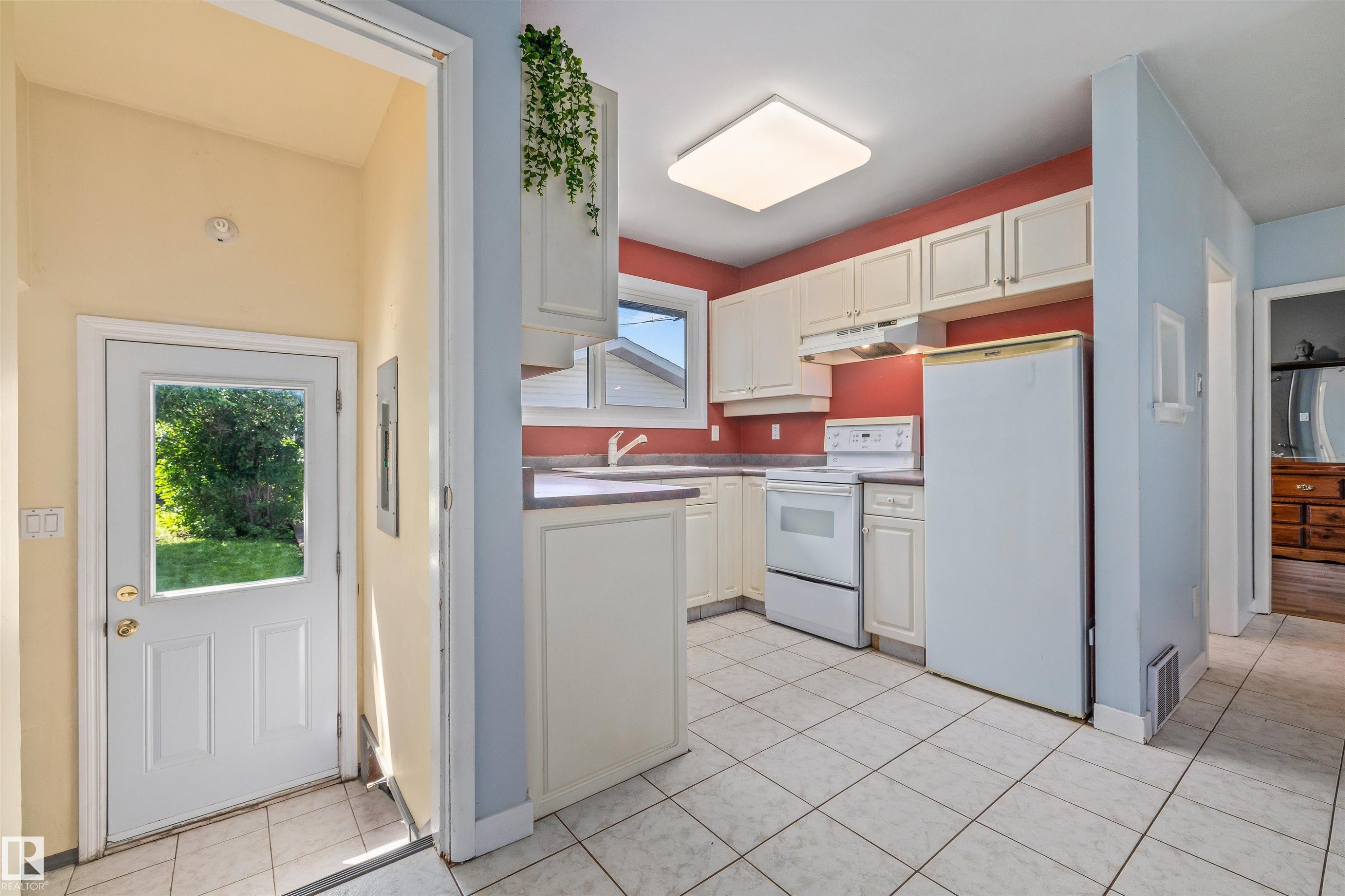 Kitchen featuring white cabinetry, white appliances, a white tile floor, and a rear door with a window providing exterior light - 13320 123 Street Nw, Edmonton, AB - Indoor Photo Showing Kitchen