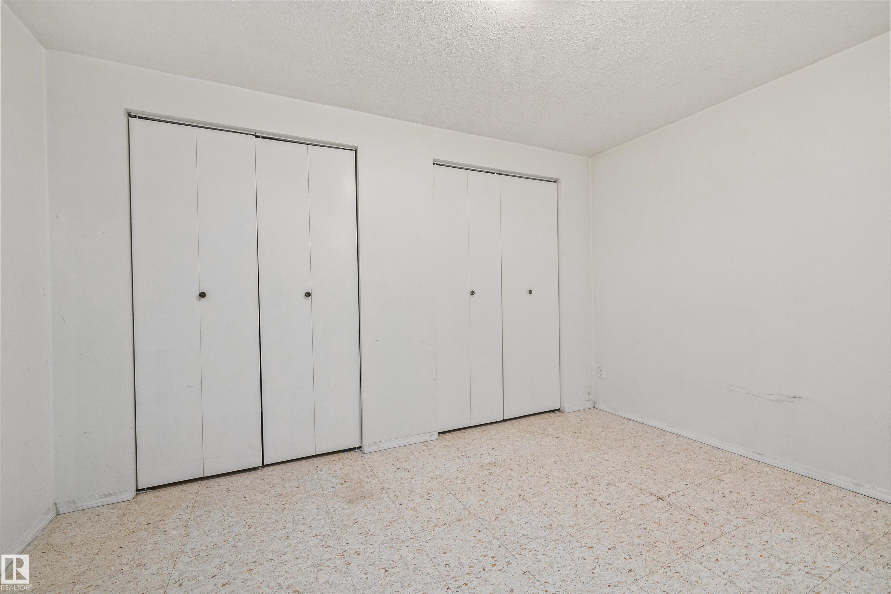 Two bi-fold closet doors with black hardware, light-colored walls, and speckled flooring - 13320 123 Street Nw, Edmonton, AB - Indoor Photo Showing Other Room